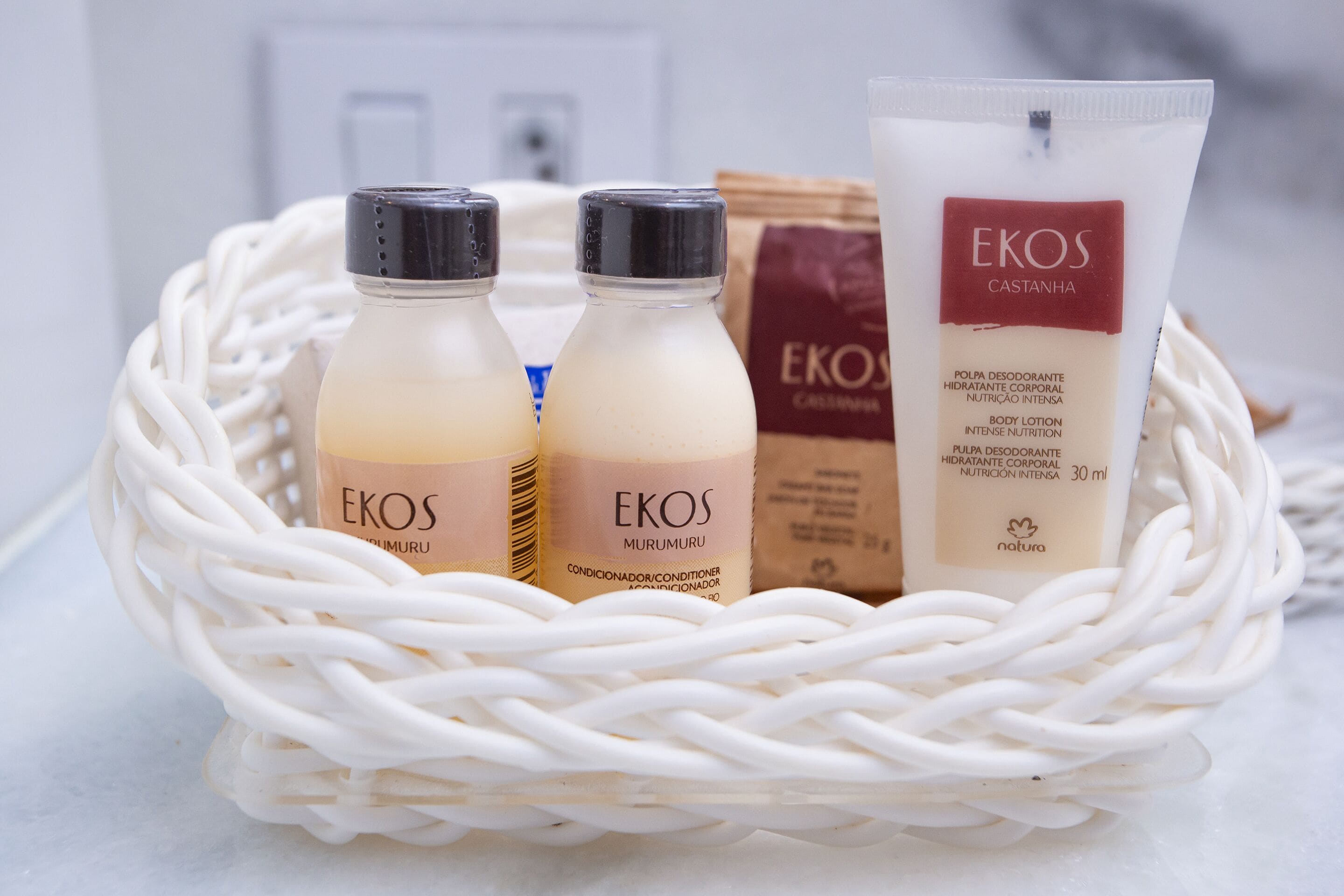 A wicker basket containing three bottles of EKOS body lotion and a tube of EKOS body lotion.