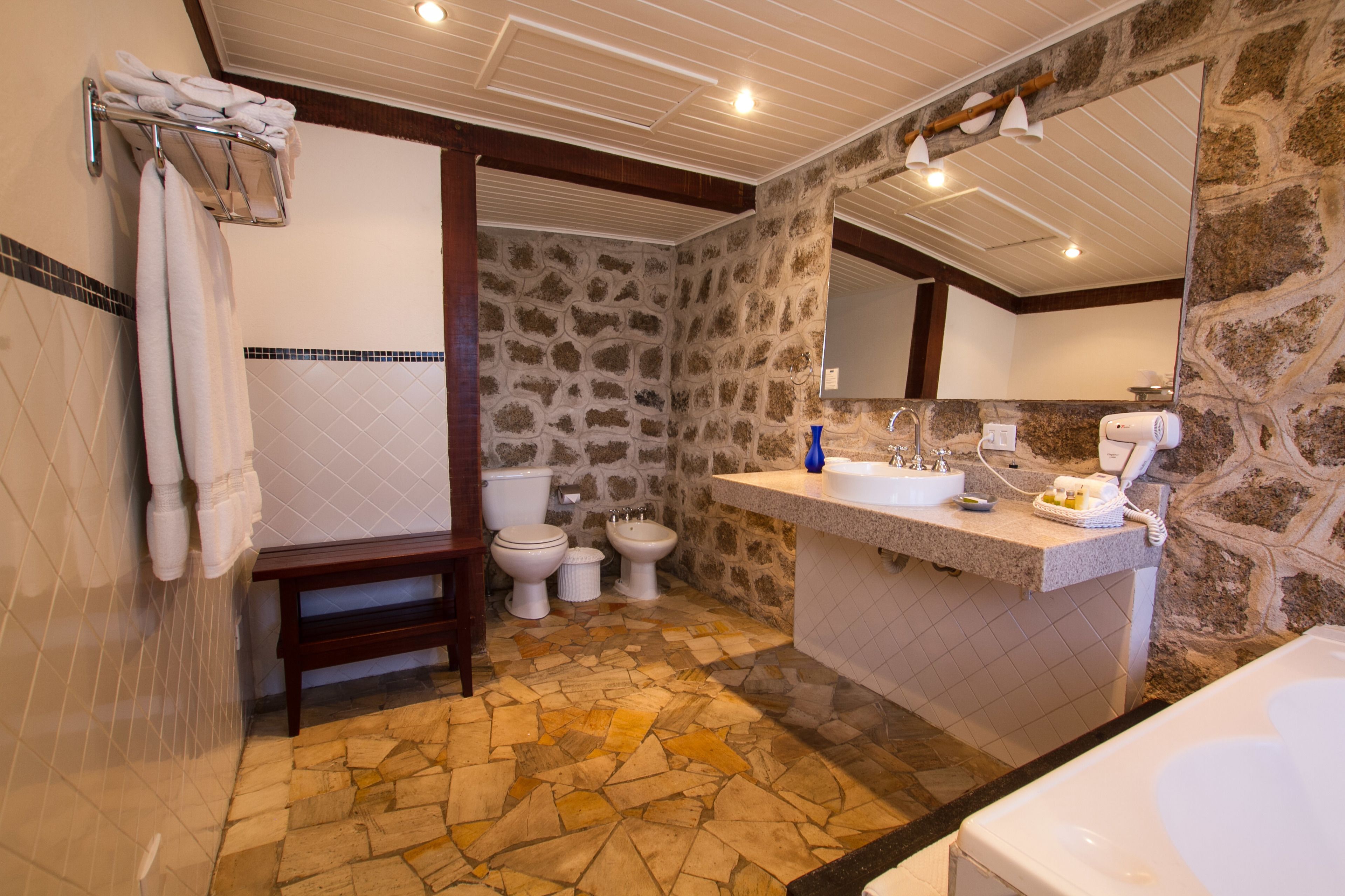 A bathroom with a stone wall, a wooden bench, a sink, and a toilet.