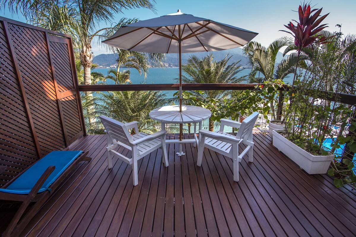 Een houten terras met een tafel, stoelen, een parasol en uitzicht op zee.
