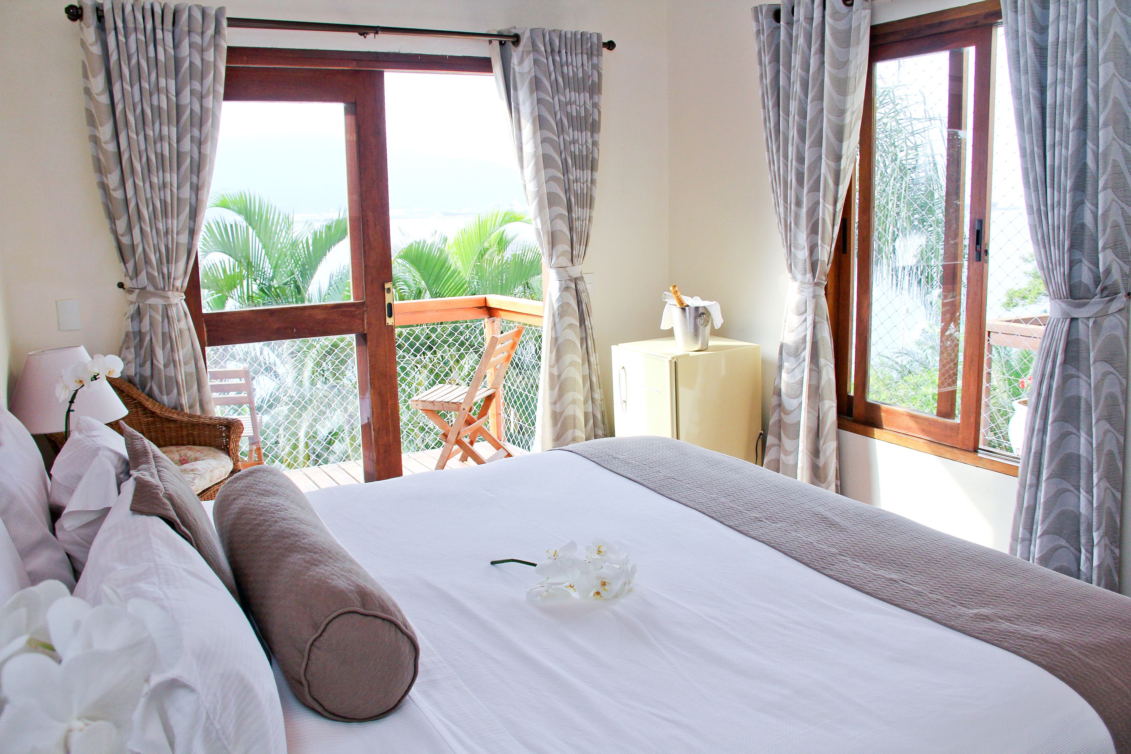 A bedroom with a large bed, a view of the outdoors, and a small table with a lamp.