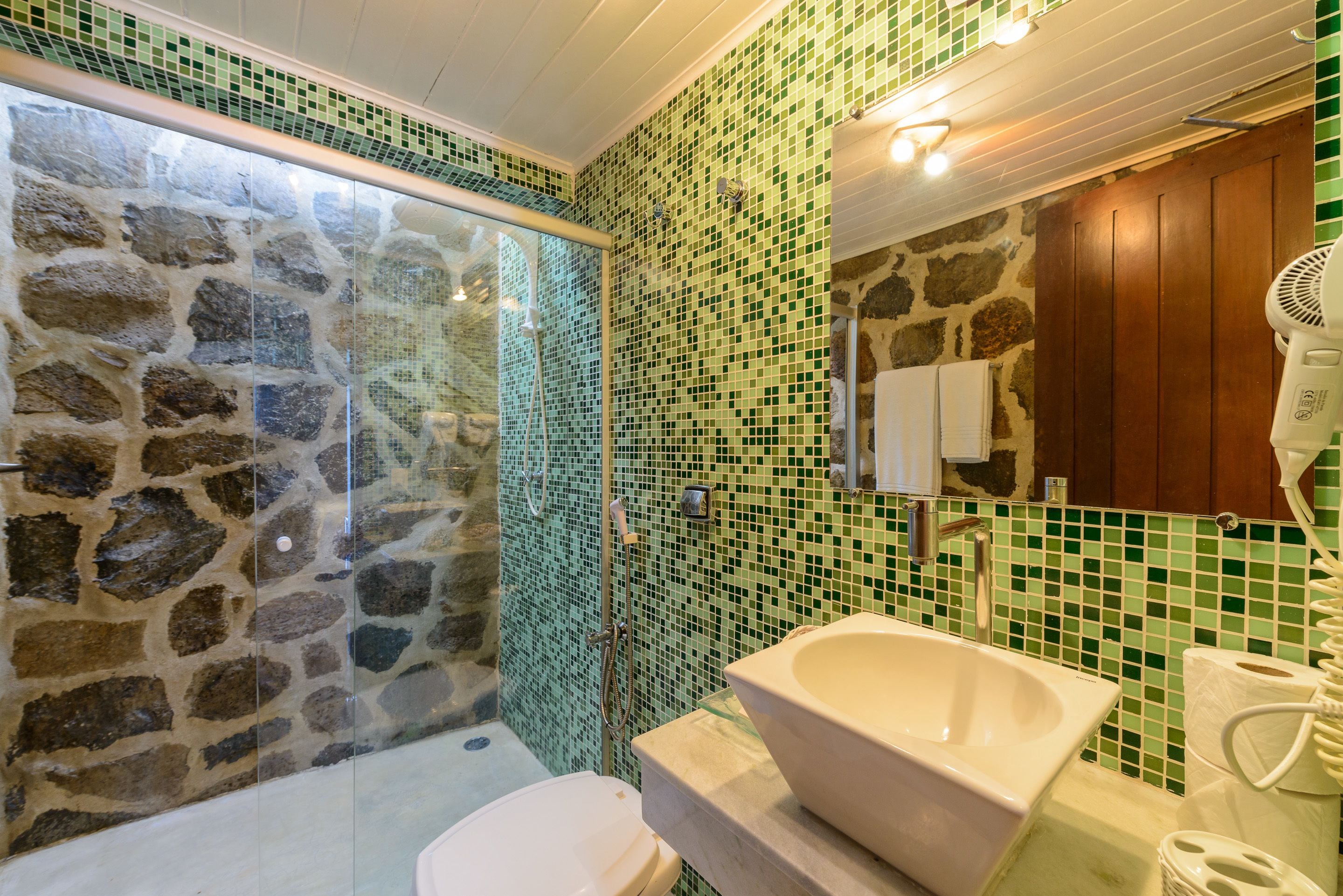 A bathroom with a stone shower enclosure, a freestanding sink, and a wooden cabinet.