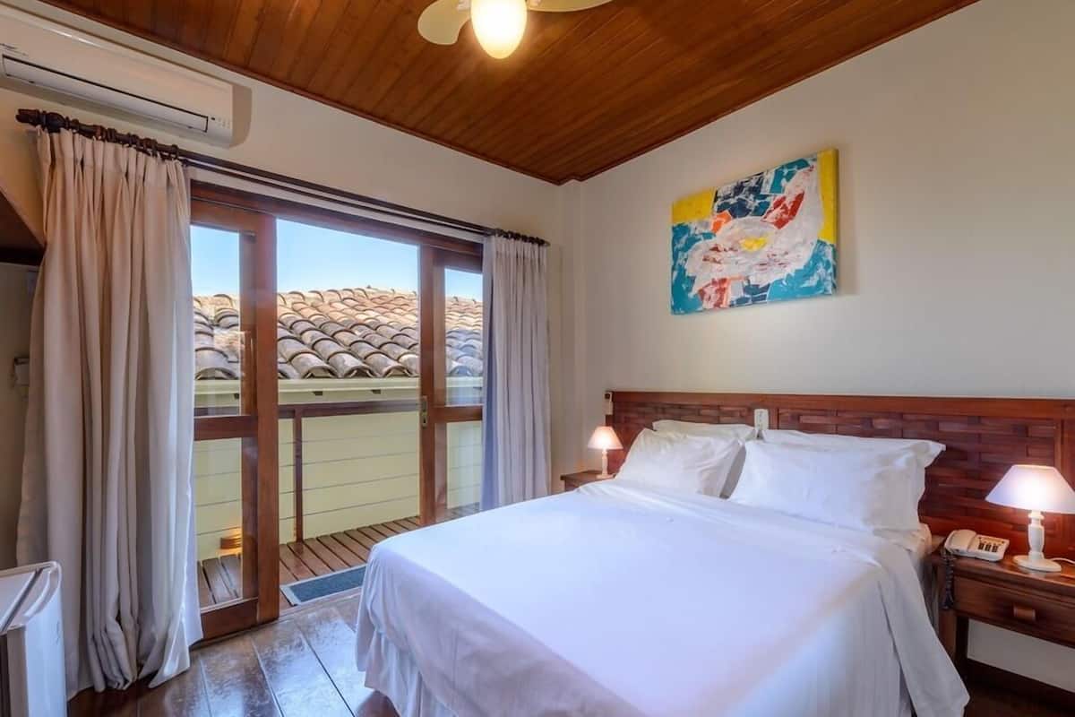 Hotelkamer met een groot bed, houten plafond en uitzicht op een pannendak door een schuifdeur.