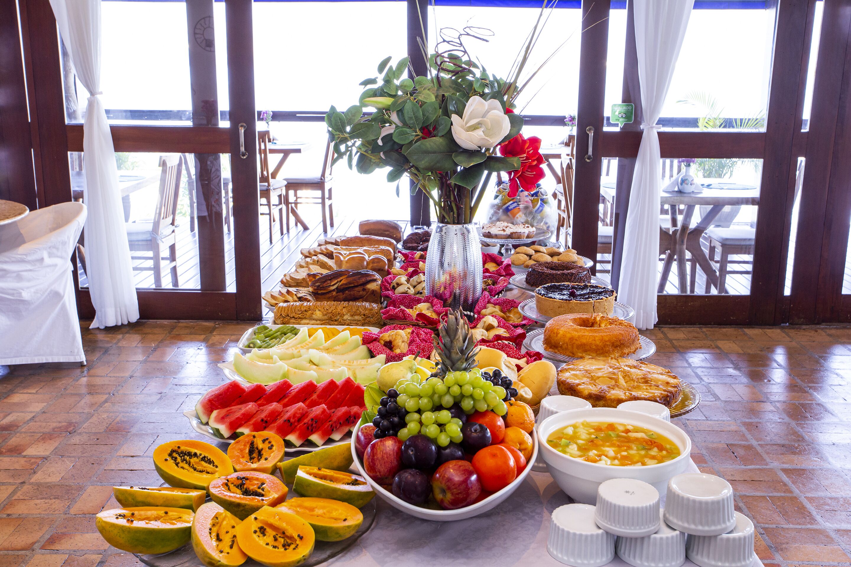 Una mesa de bufé con una variedad de frutas, pasteles y un centro de mesa con flores.