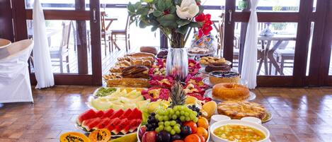 A buffet table with a variety of fruits, pastries, and a centerpiece with flowers.