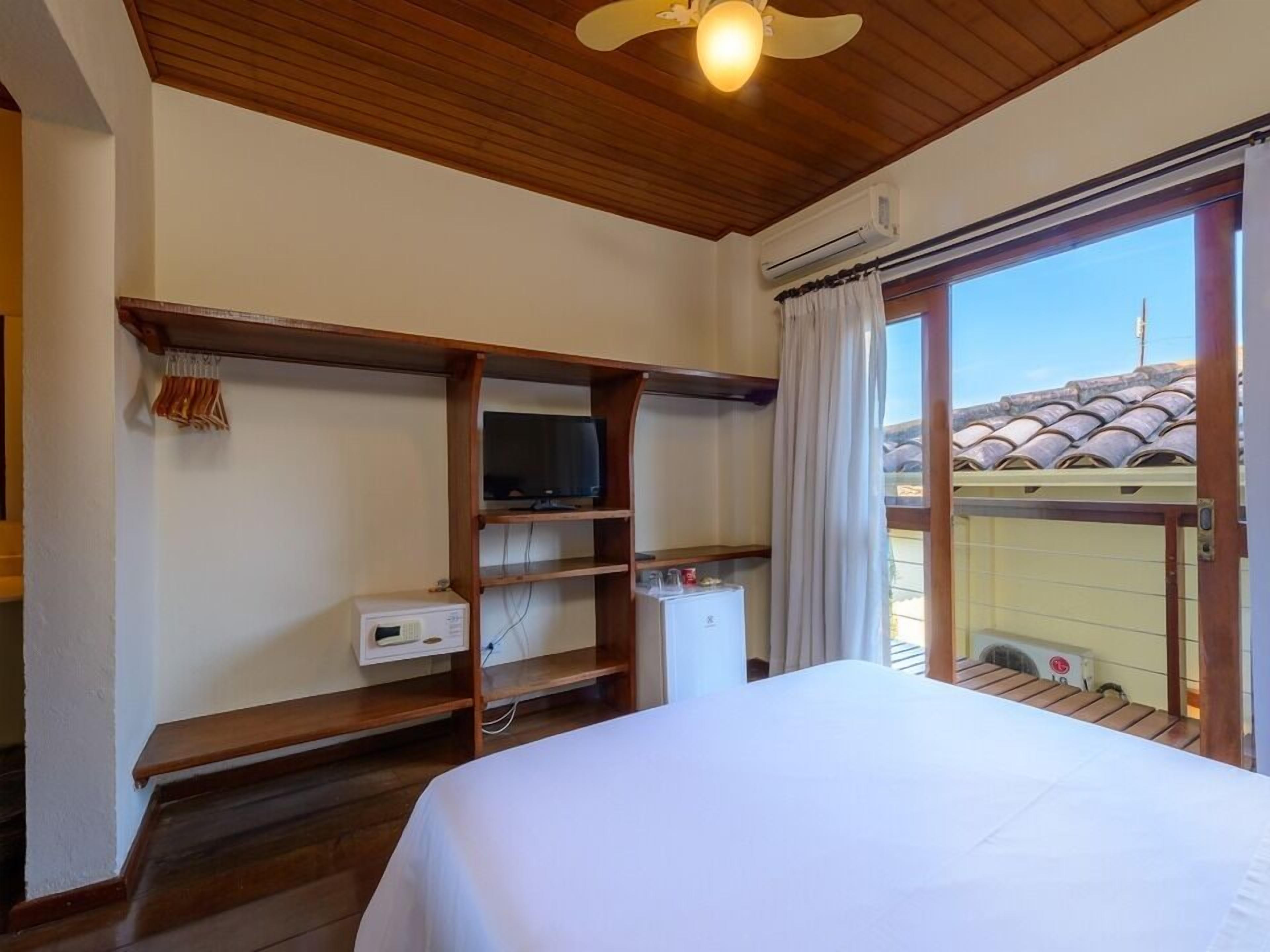 Een hotelkamer met een bed, een televisie op een plank, een kleine koelkast en een raam met gordijnen.