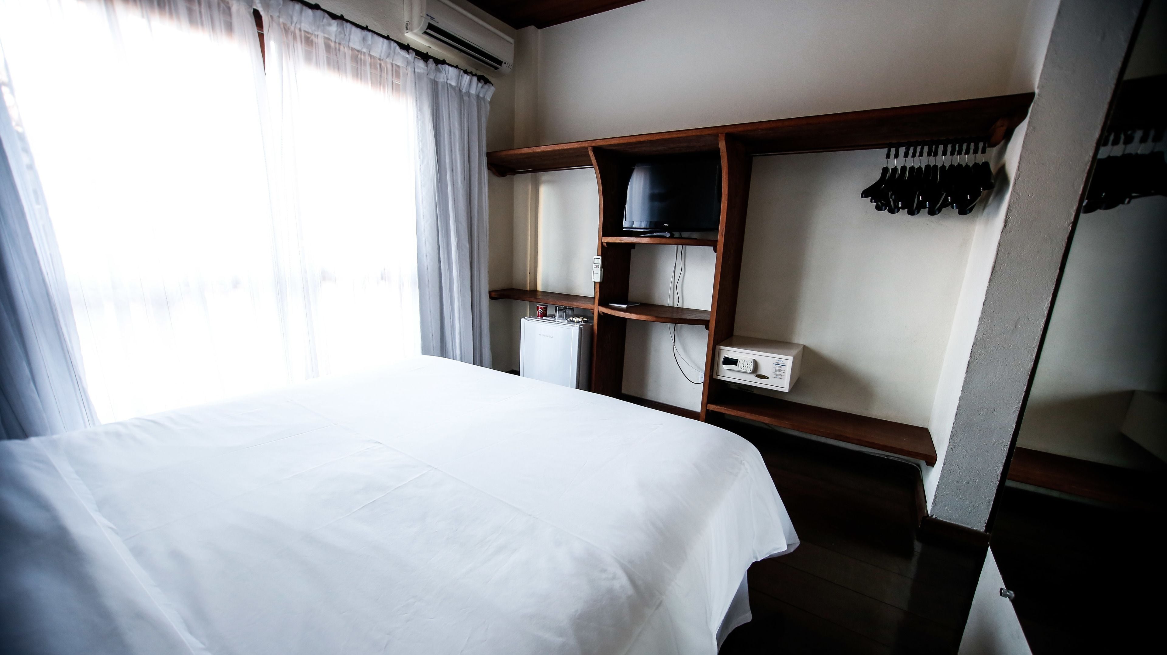A hotel room with a bed, a wardrobe, a heater, and a shelf with clothes.