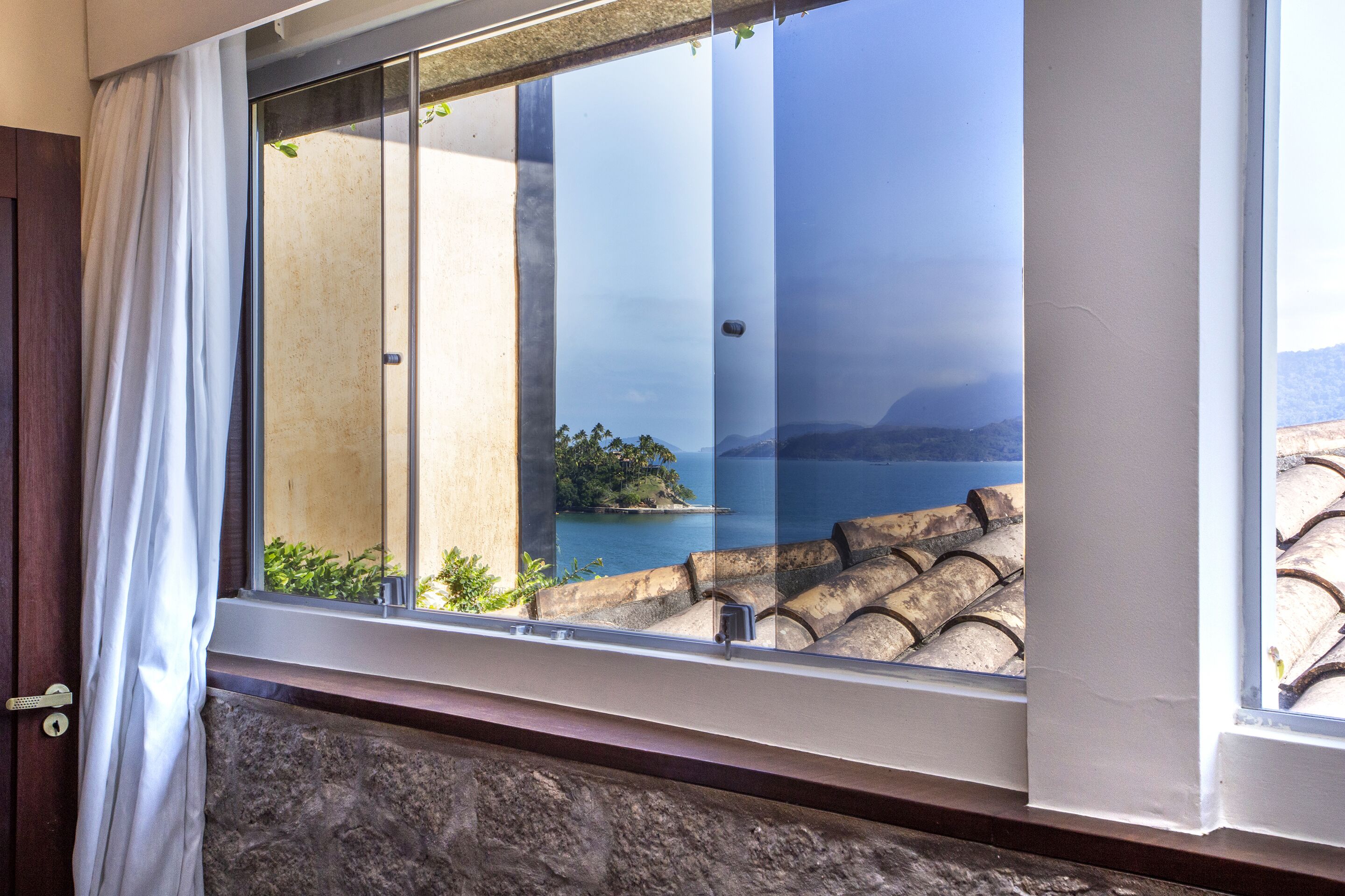 A room with a large window overlooking a scenic view of a body of water and distant mountains.