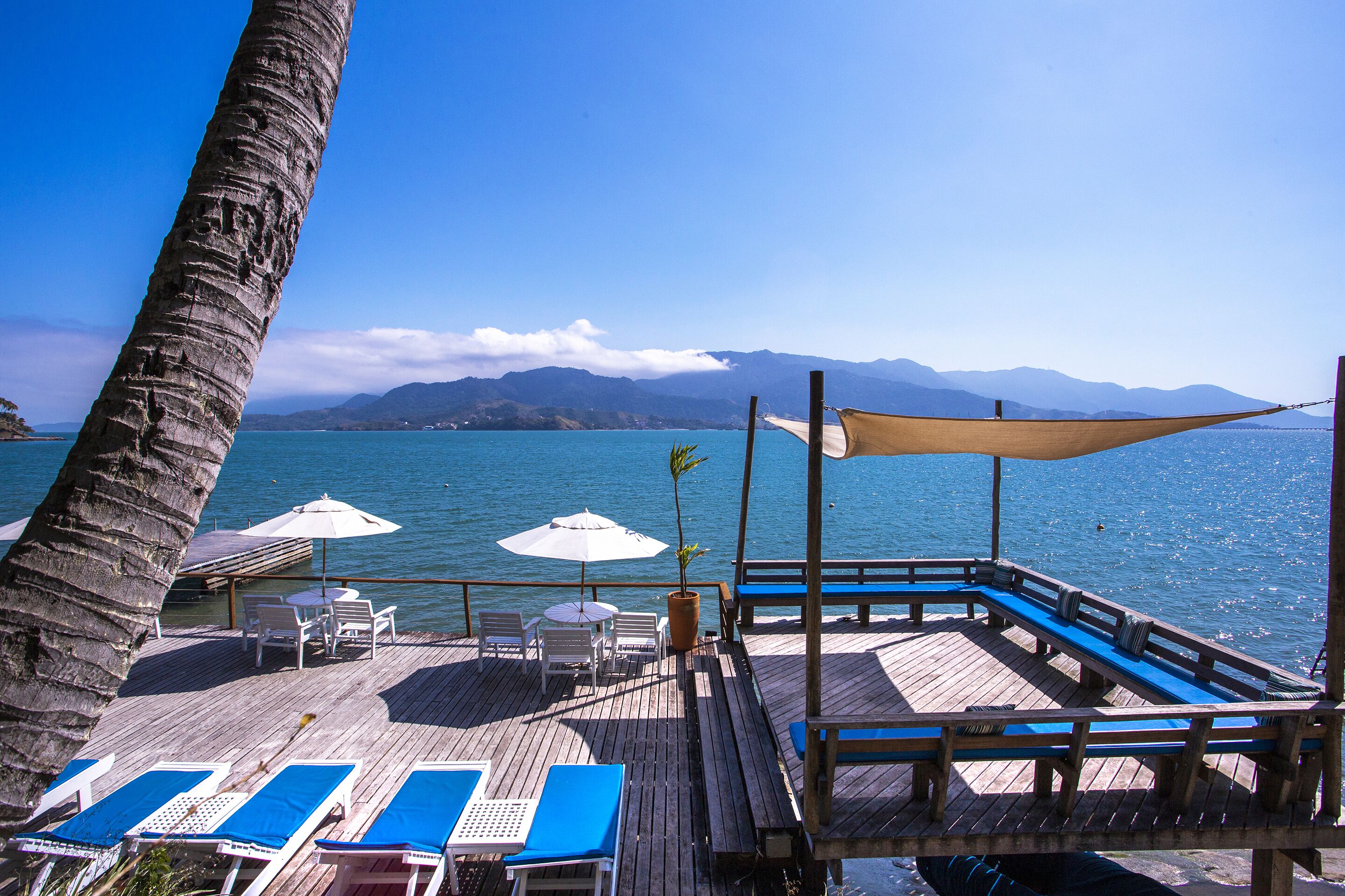 A wooden deck with lounge chairs and umbrellas overlooking a body of water with mountains in the background.