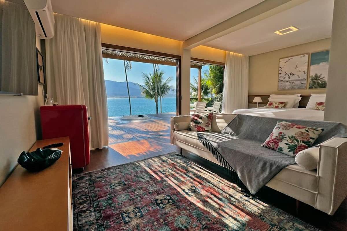 Een hotelkamer met een groot bed, een bank, een tafeltje en uitzicht op zee.