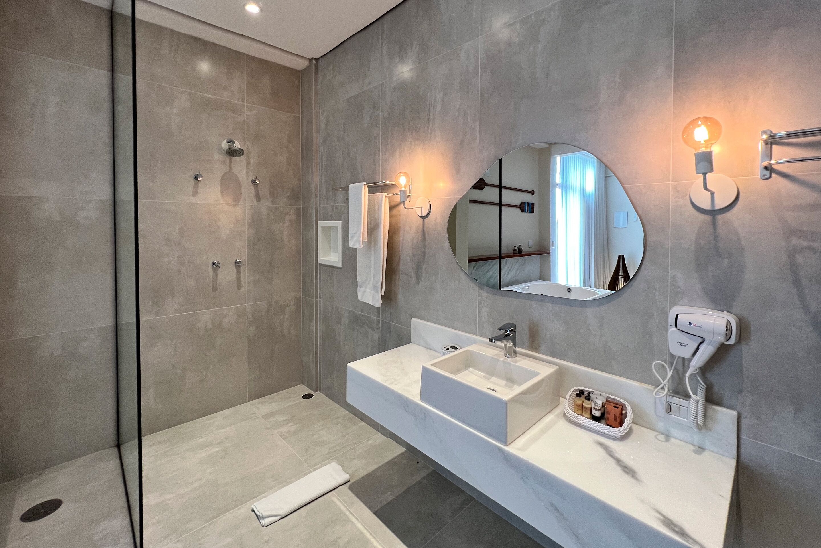 Un baño moderno con cabina de ducha de vidrio, un espejo grande y tocador con lavabo y perchero para toallas.