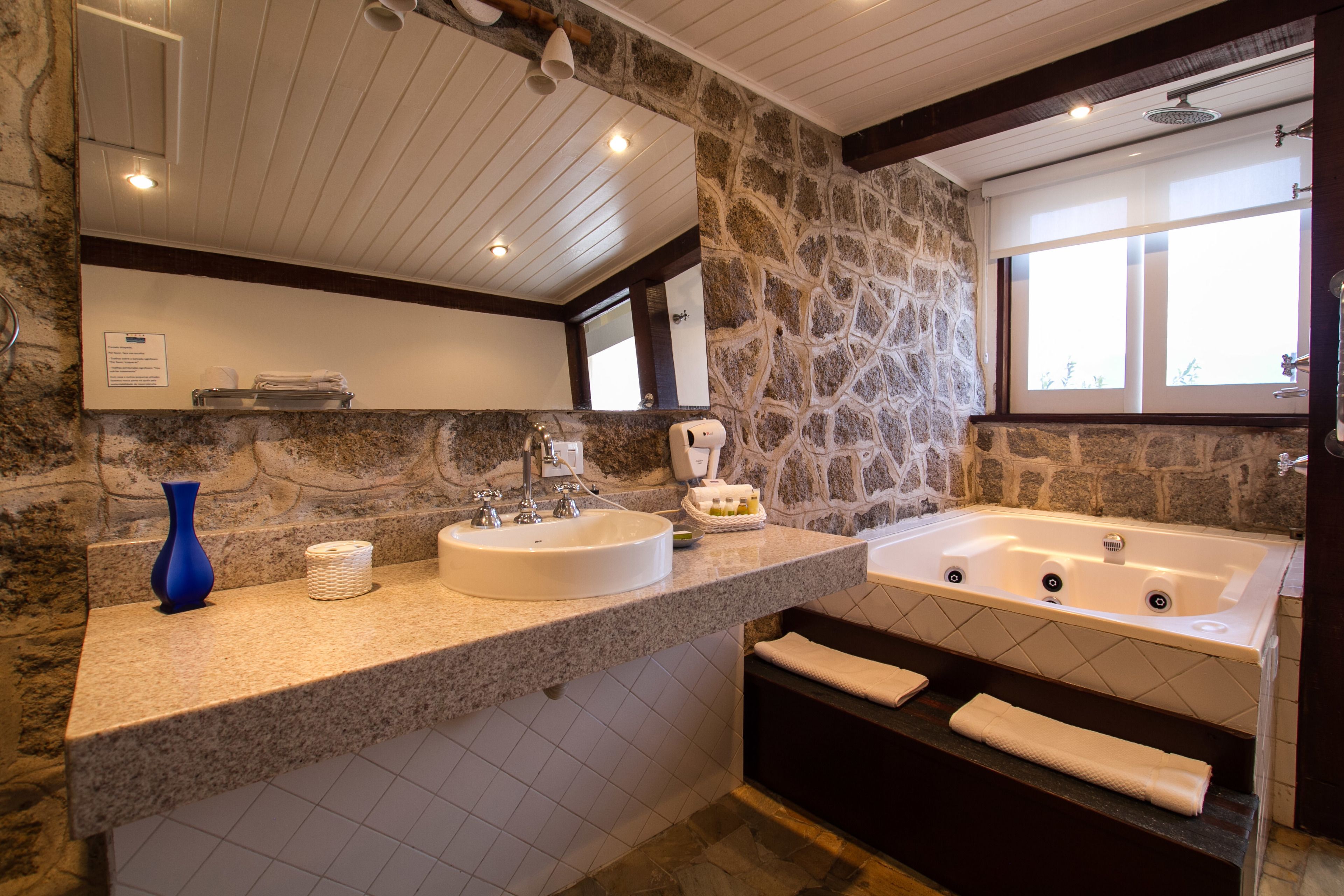 A bathroom with a stone wall, two sinks, a bathtub, and a window.