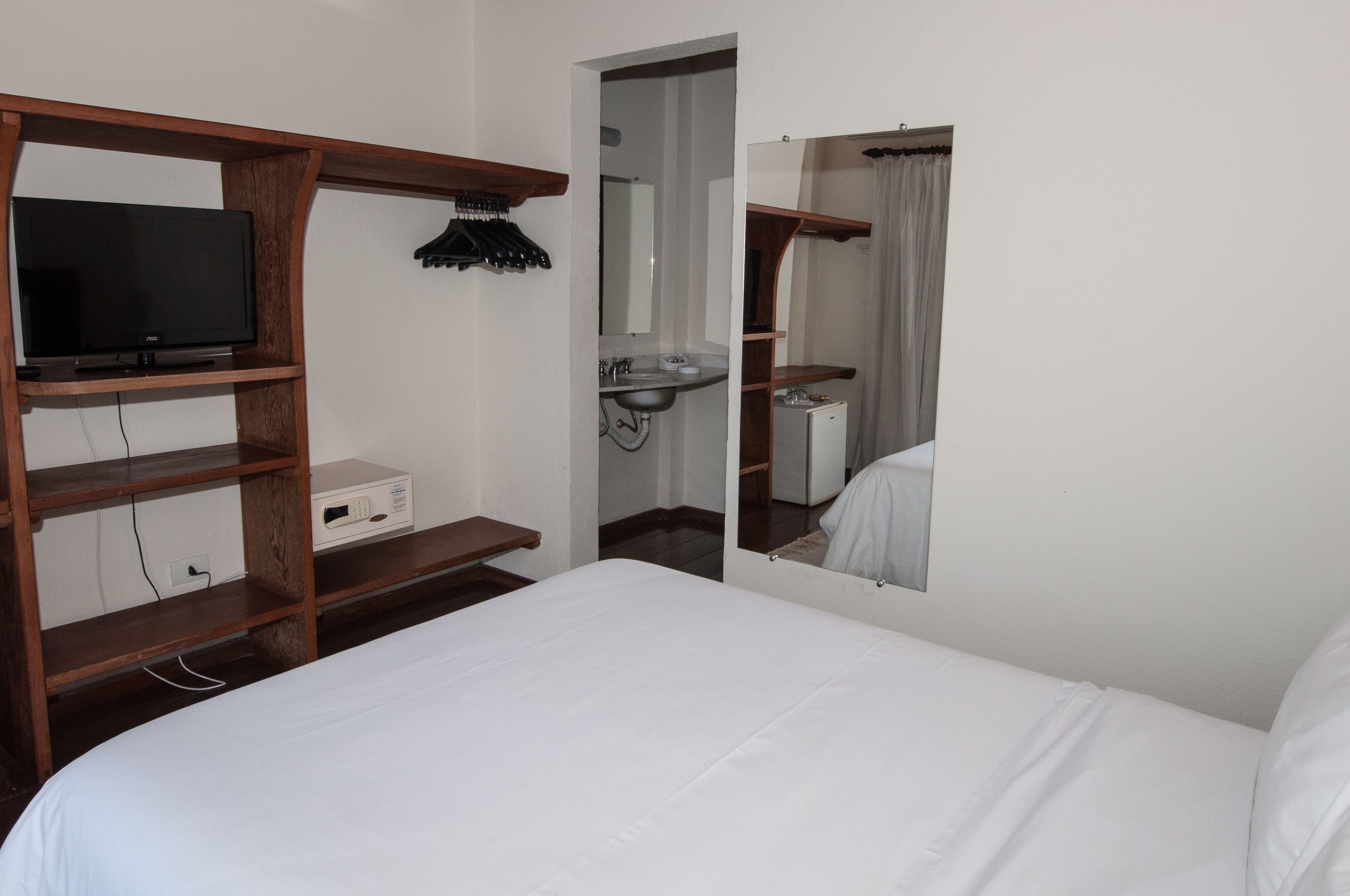 Habitación de hotel con cama, televisor sobre una estantería de madera, baño con lavamanos y espejo, y cortina de ducha.