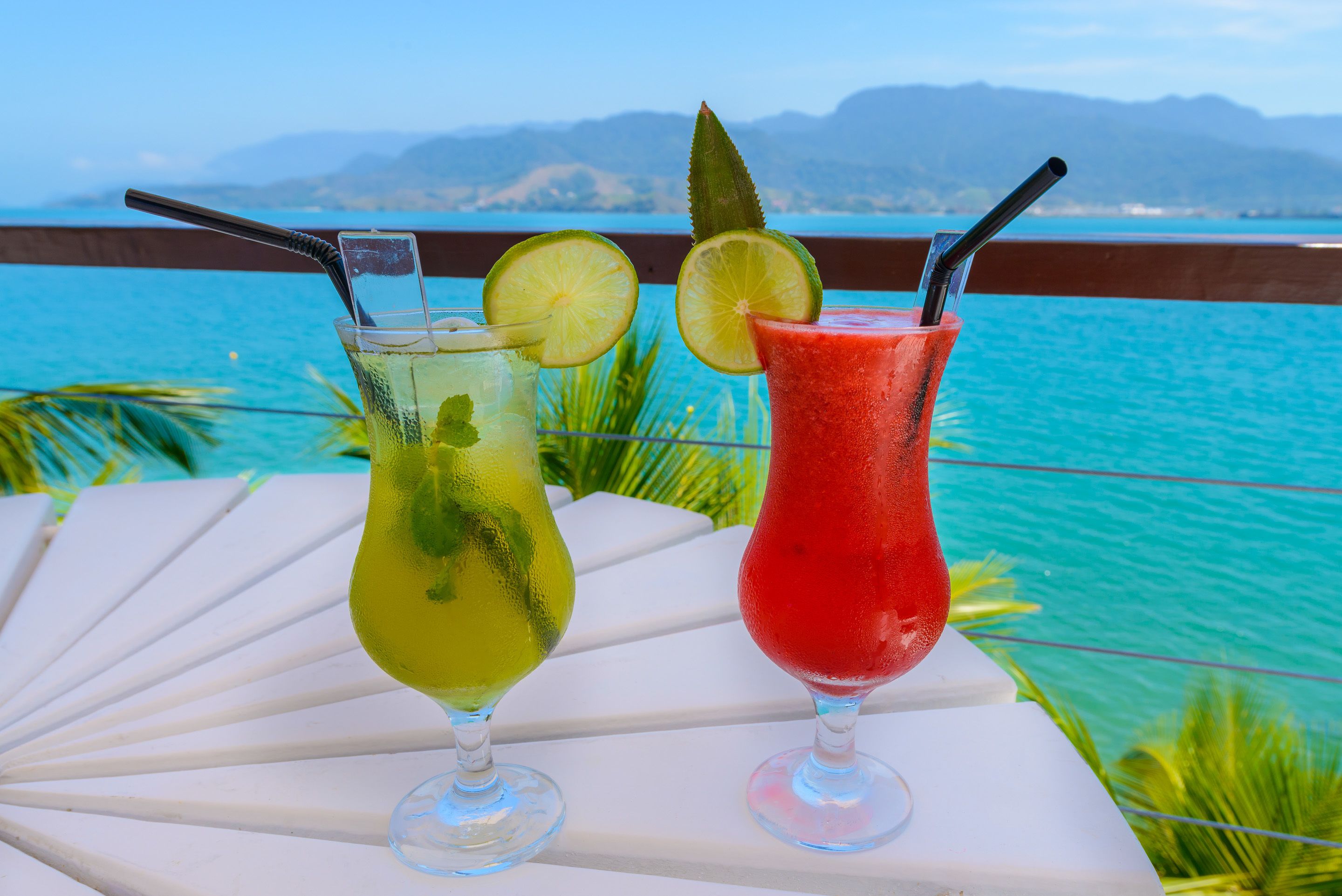 Deux cocktails sur une table blanche, avec une vue sur l’océan et les montagnes en arrière-plan.