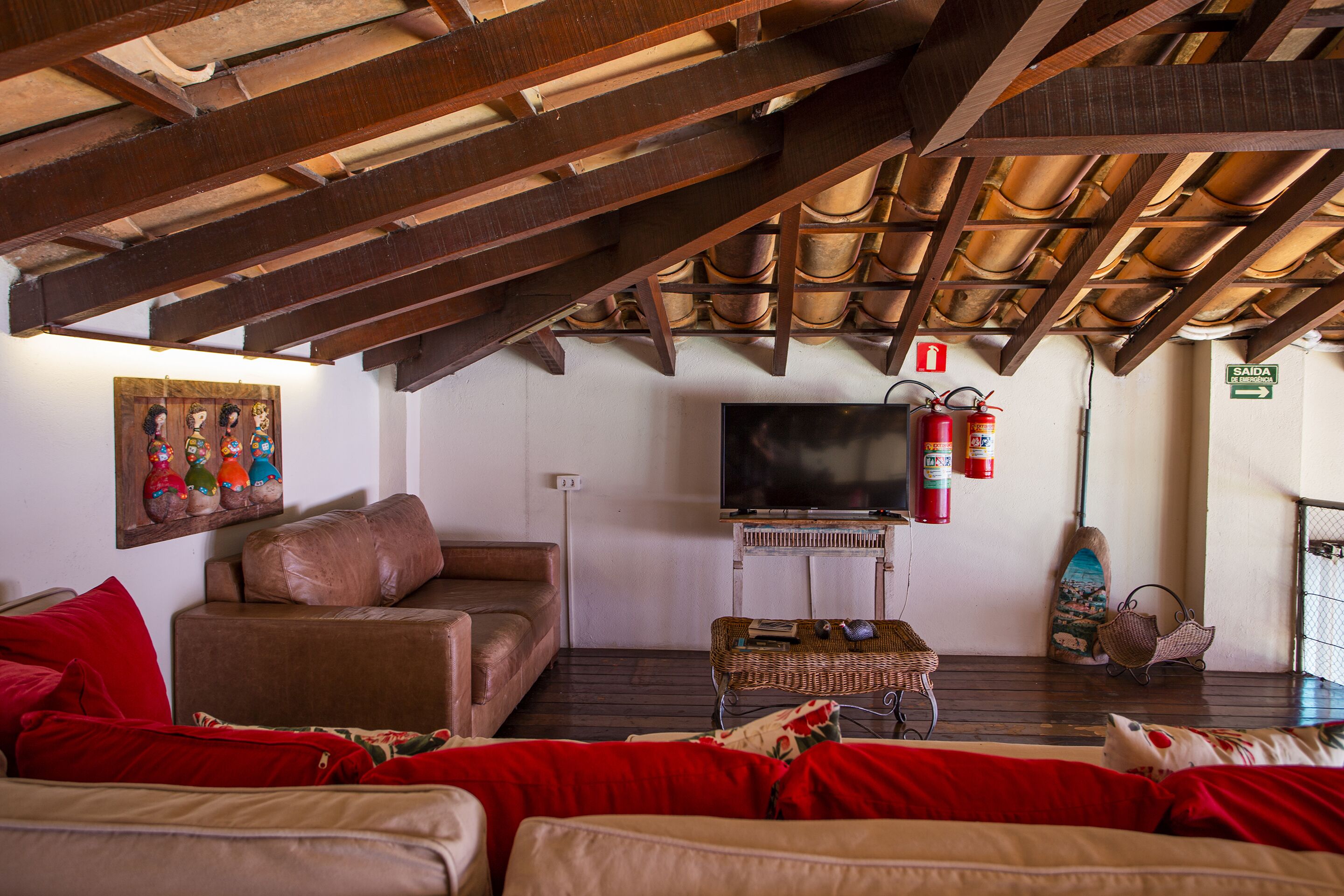 Un saló d'estar acollidor amb un sofà de pell marró, coixins vermells, un televisor de pantalla plana i un sostre de fusta.