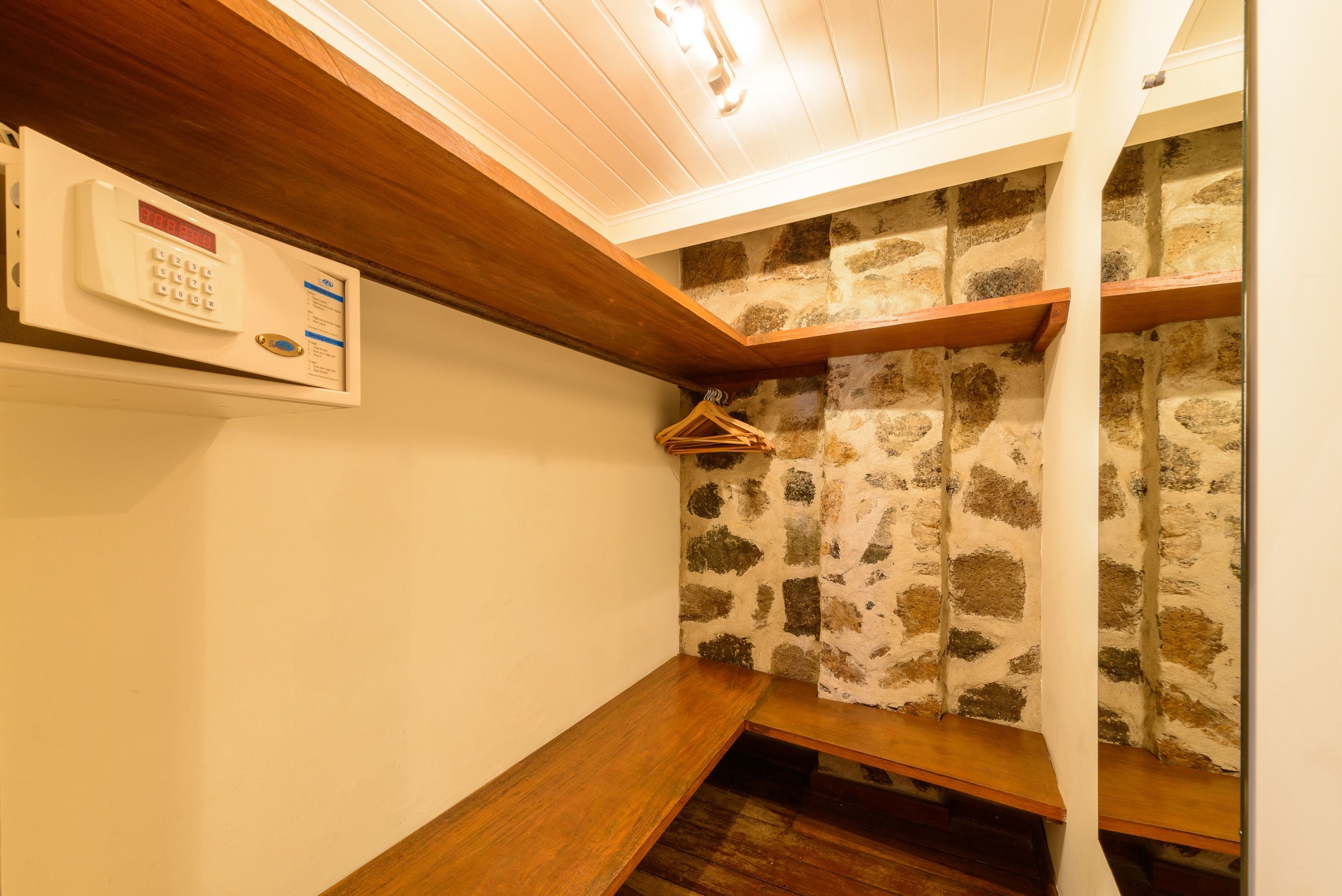 Una esquina de habitación con un banco de madera, un panel de seguridad fijado a la pared y un muro de piedra.