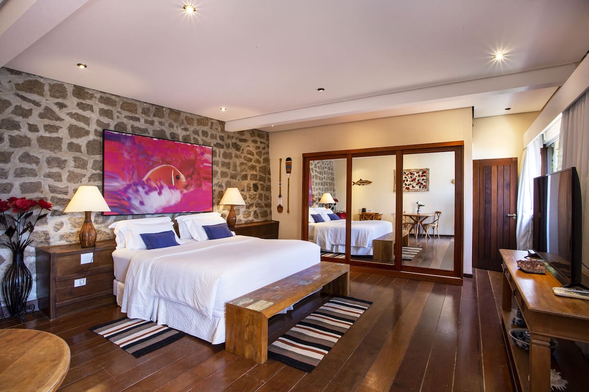 Een goed verlichte slaapkamer met een groot bed, nachtkastjes, een houten bankje en een televisie.