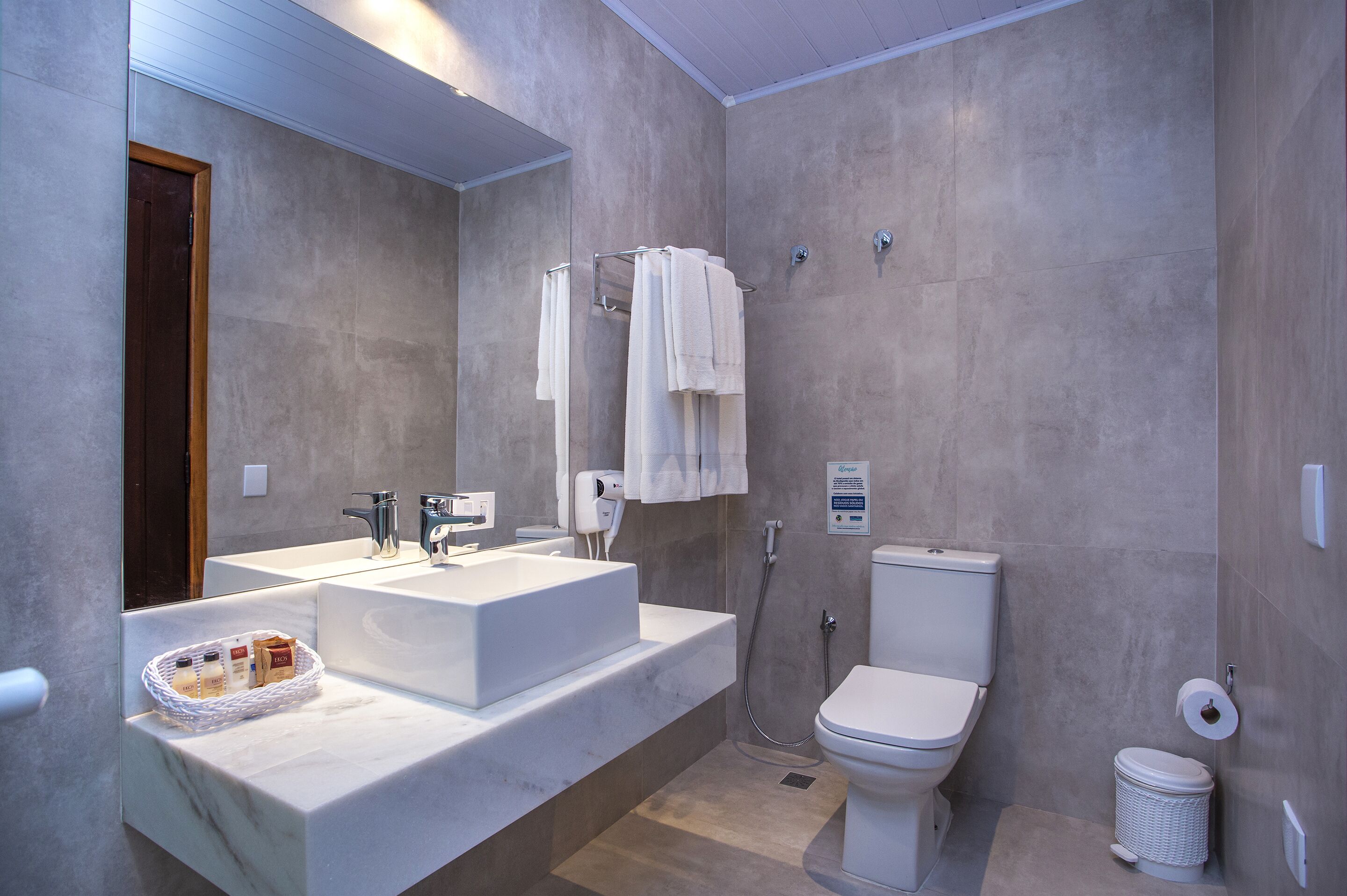 A modern bathroom with a large mirror, a white sink, a toilet, and a shower area.