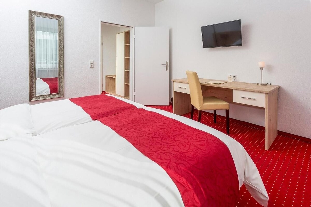 A hotel room with a bed, a desk, a chair, a television, and a wardrobe.