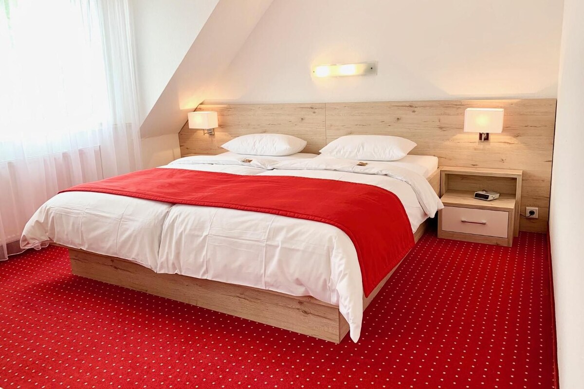 A bedroom with a wooden bed, white bedding, red polka dot carpet, and two bedside tables with lamps.