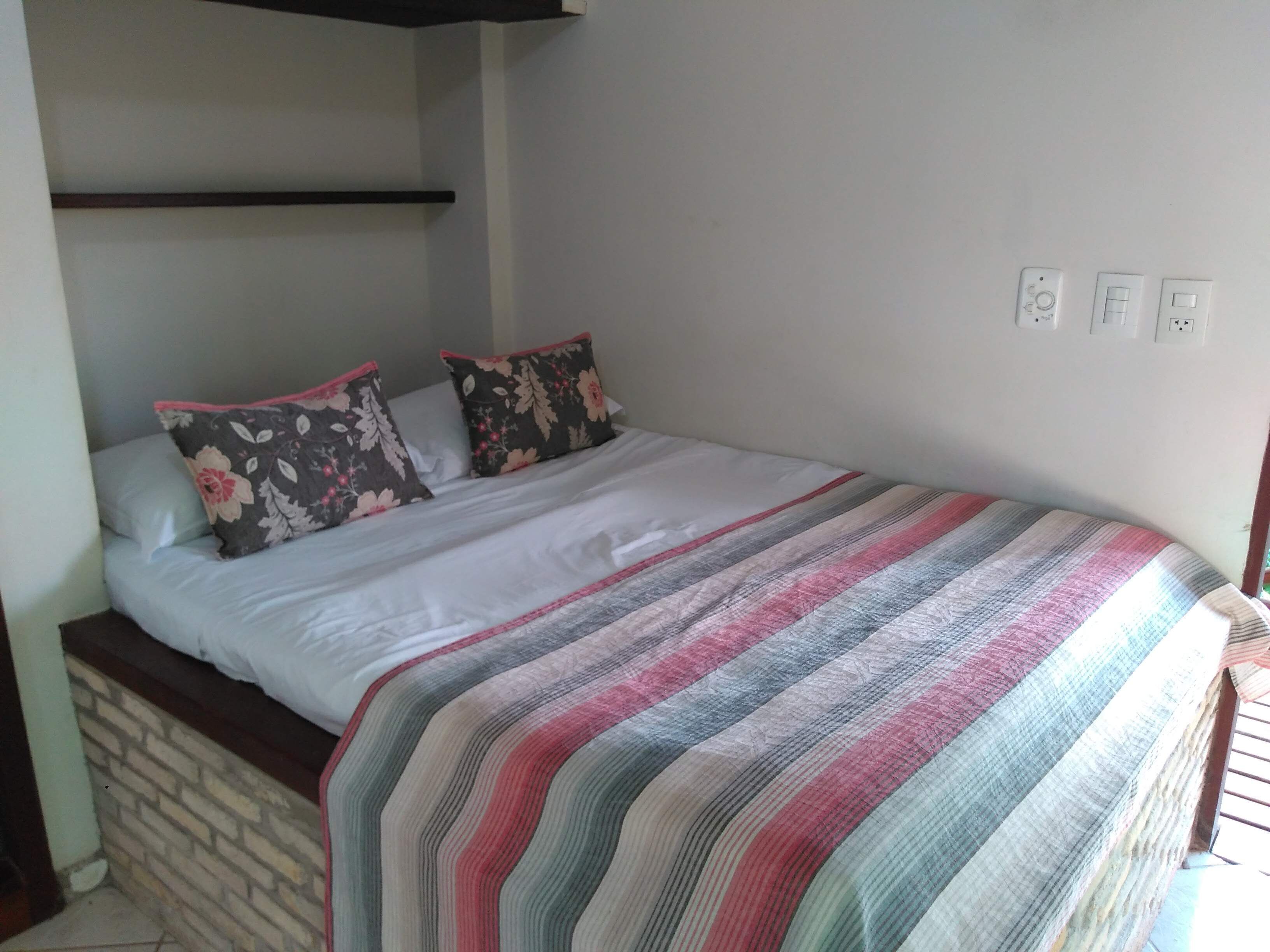 A bed with a striped blanket, two floral pillows, and a wooden headboard.