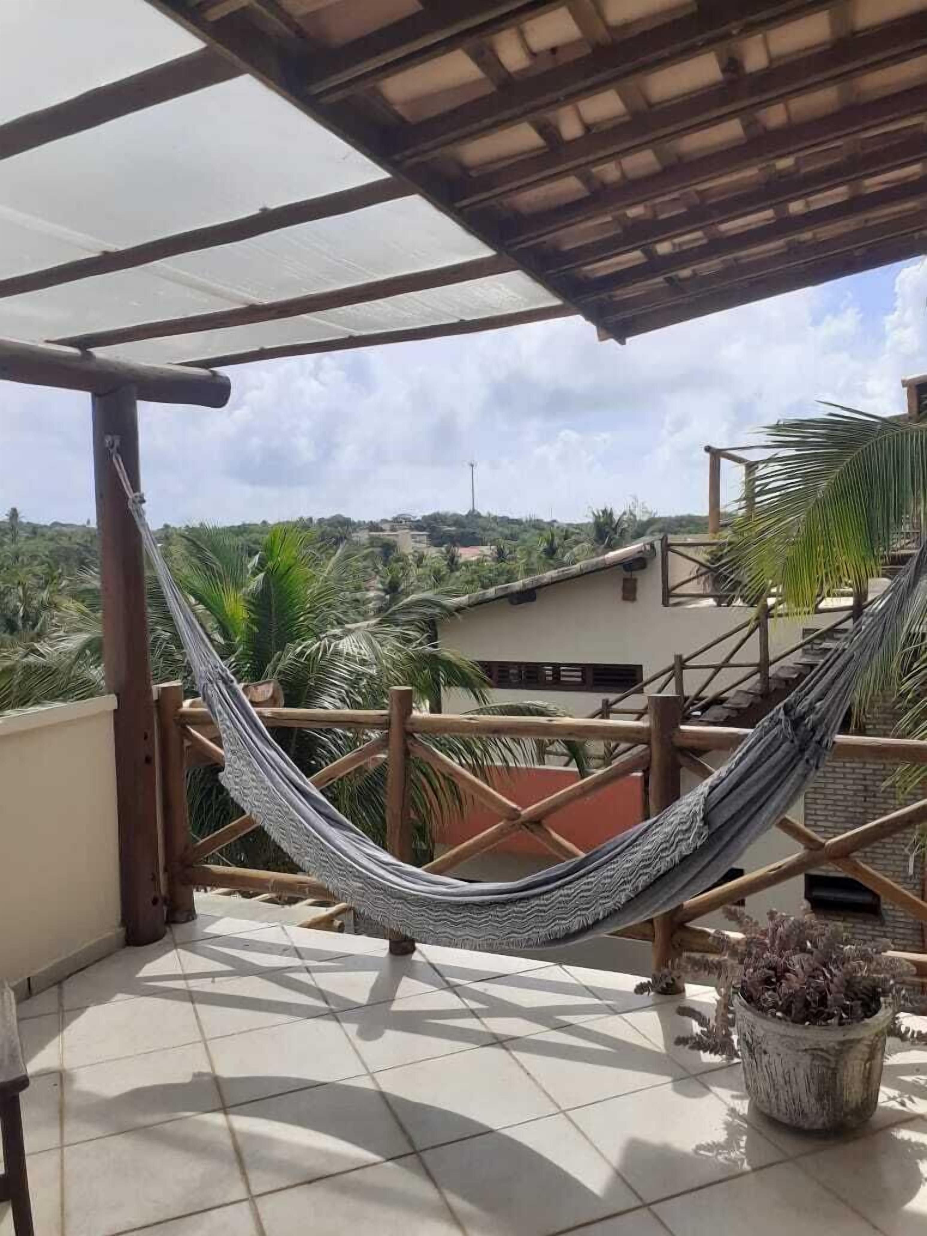 Una hamaca en un balcón con baldosas, con vista a una zona residencial y una palmera.