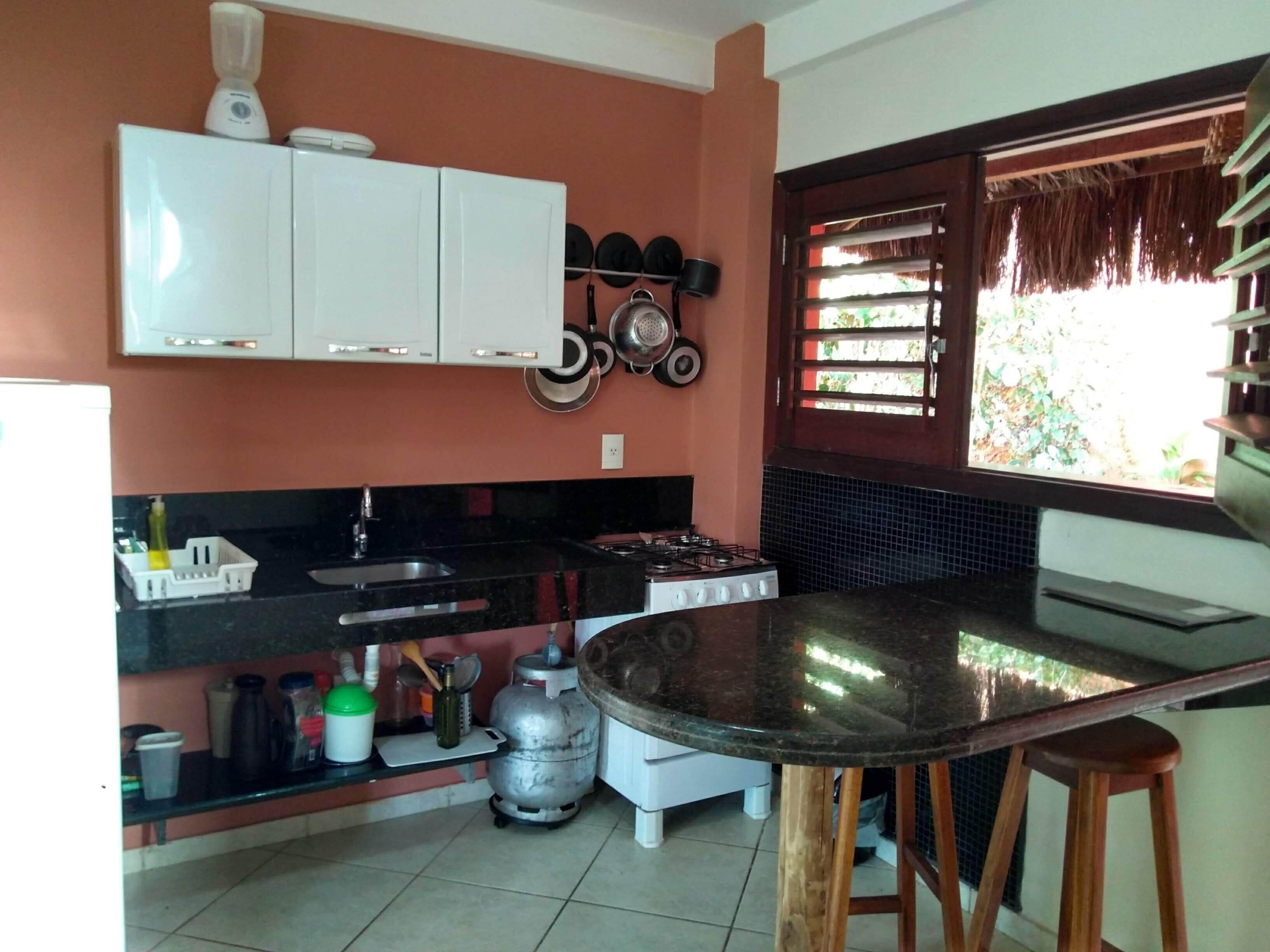 A compact kitchen with white cabinets, a gas stove, a sink, and a small dining area with stools.