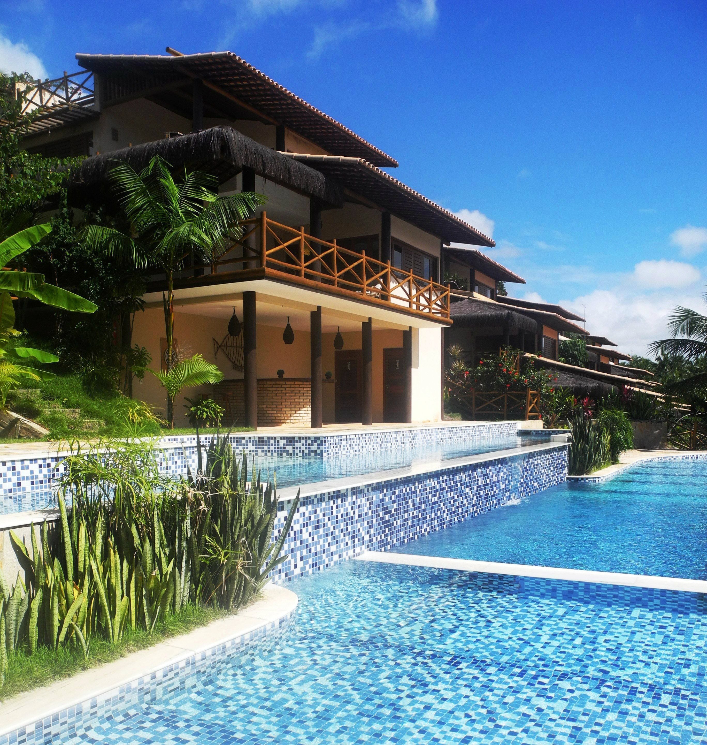 A resort with a swimming pool, a thatched-roof structure, and lush greenery.