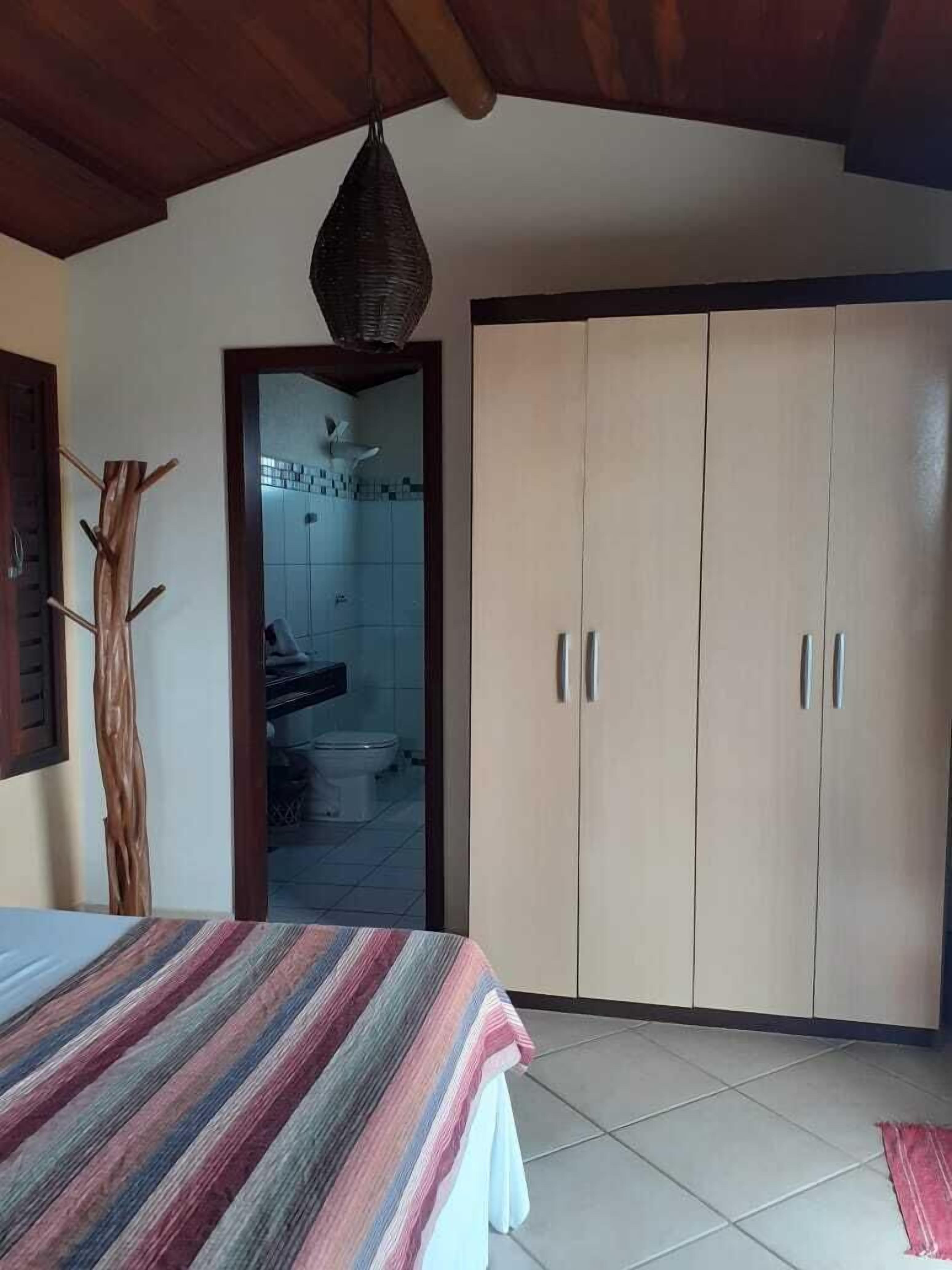 Ein Schlafzimmer mit Bett, Kleiderschrank und einem durchgehenden Türrahmen sichtbarem Badezimmer.
