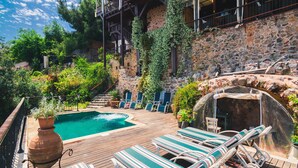 A pool area with lounge chairs, a hot tub, and a stone wall. - Hotel Villa Turka (Alanya)