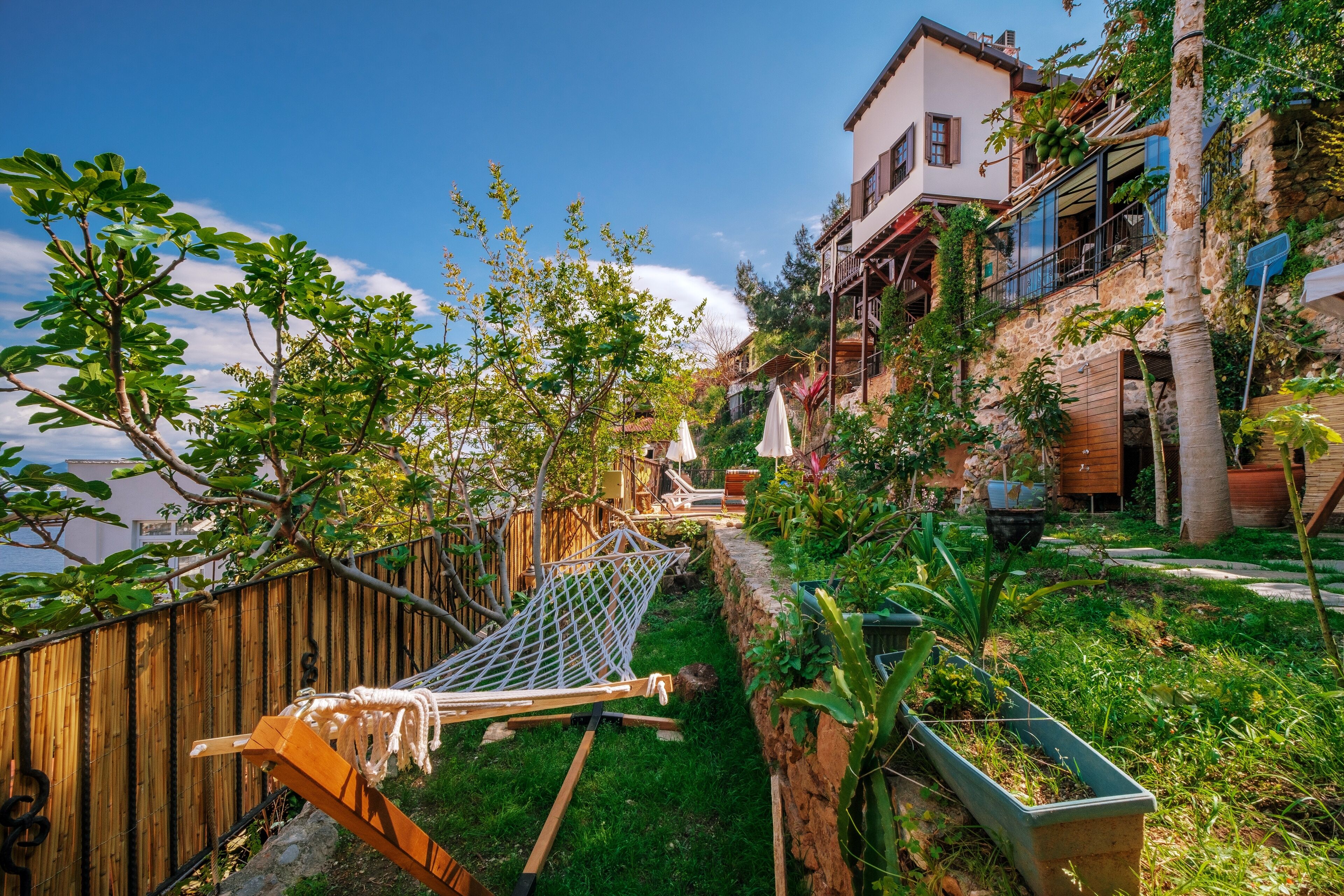 A garden with a hammock, a wooden fence, and a stone wall.