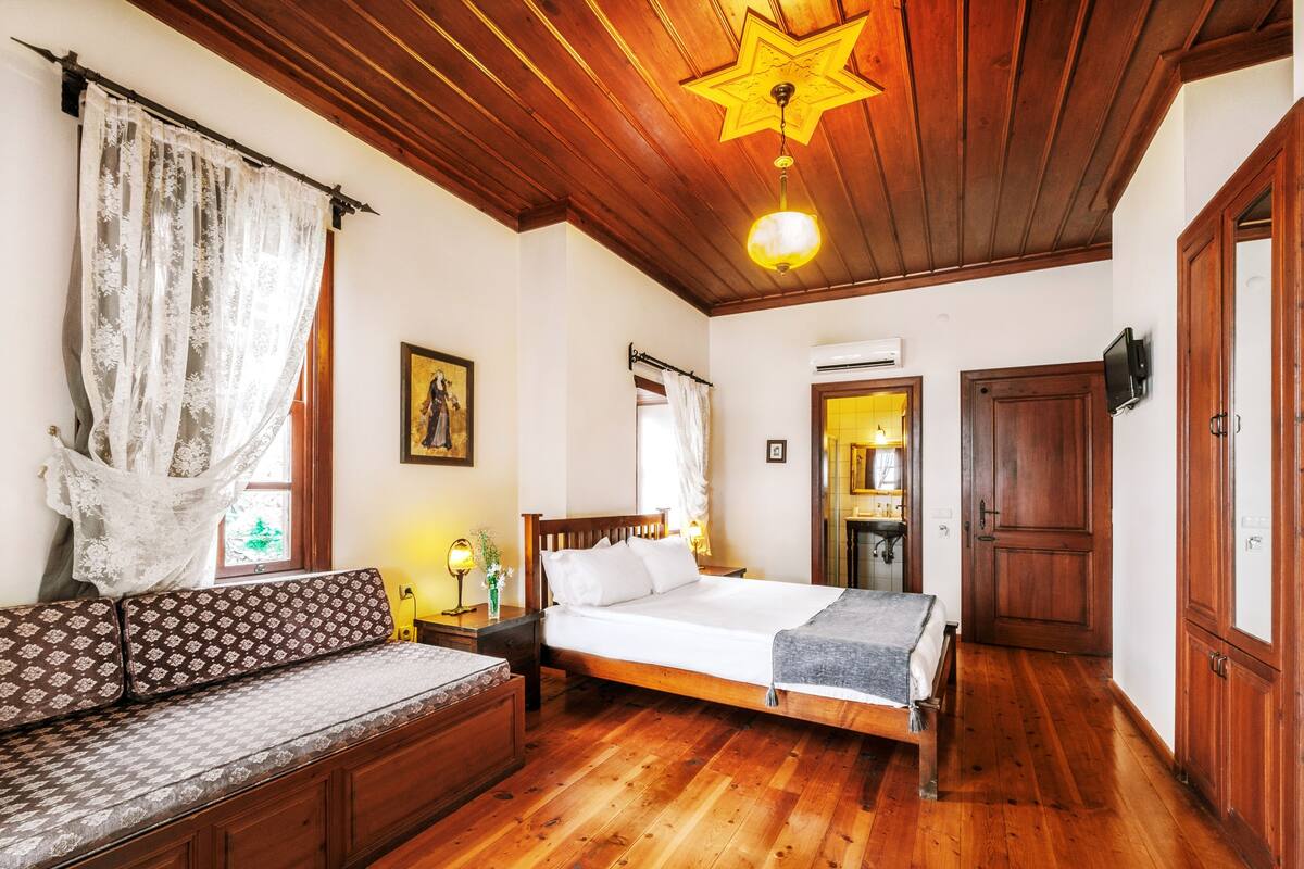 A wooden-floored bedroom with a bed, a bench, and a star-shaped ceiling light.