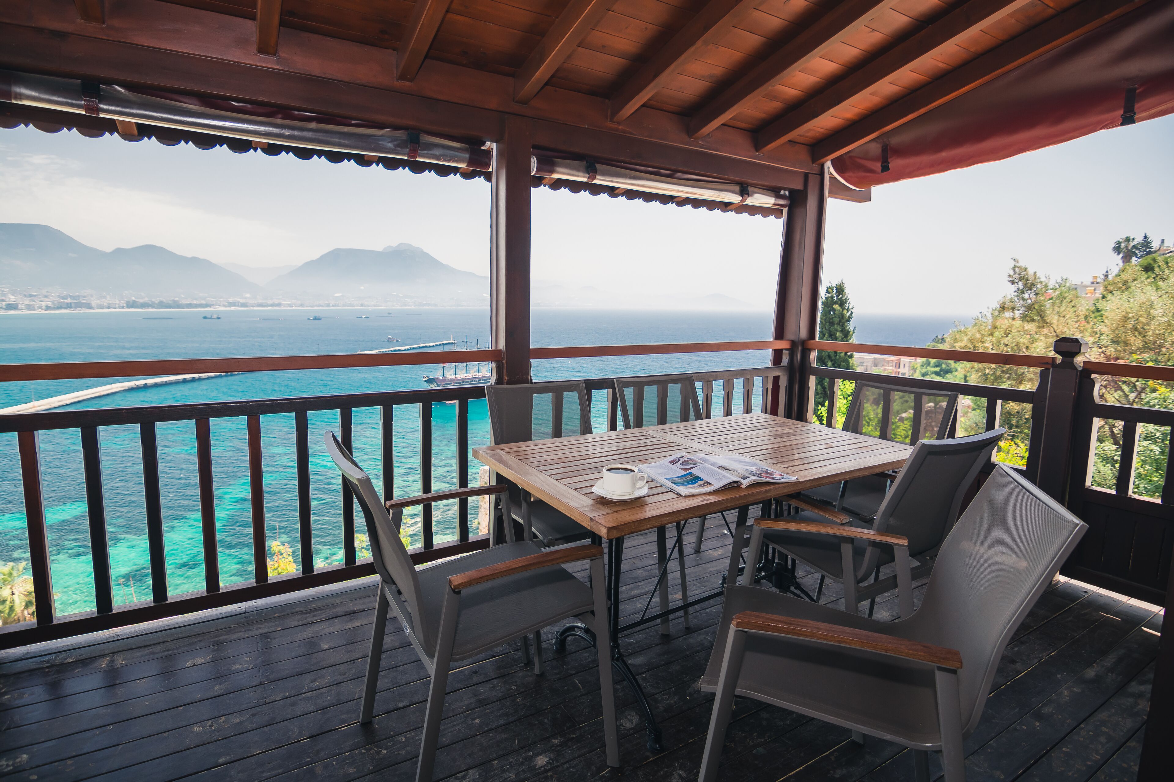 A wooden deck with a table and chairs overlooking a turquoise sea and distant mountains.