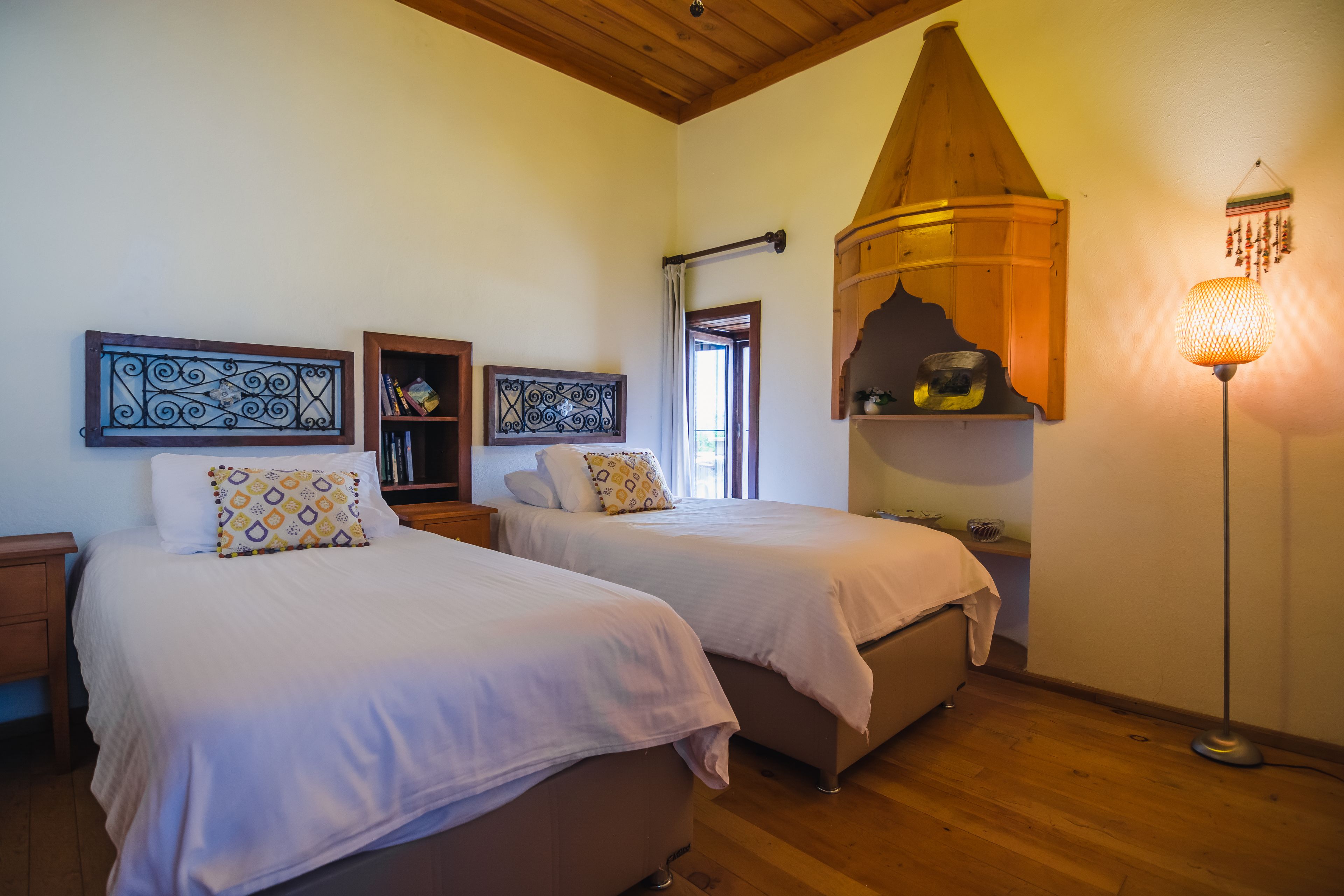 A bedroom with two beds, wooden flooring, a ceiling fan, and a wall-mounted shelf with books.