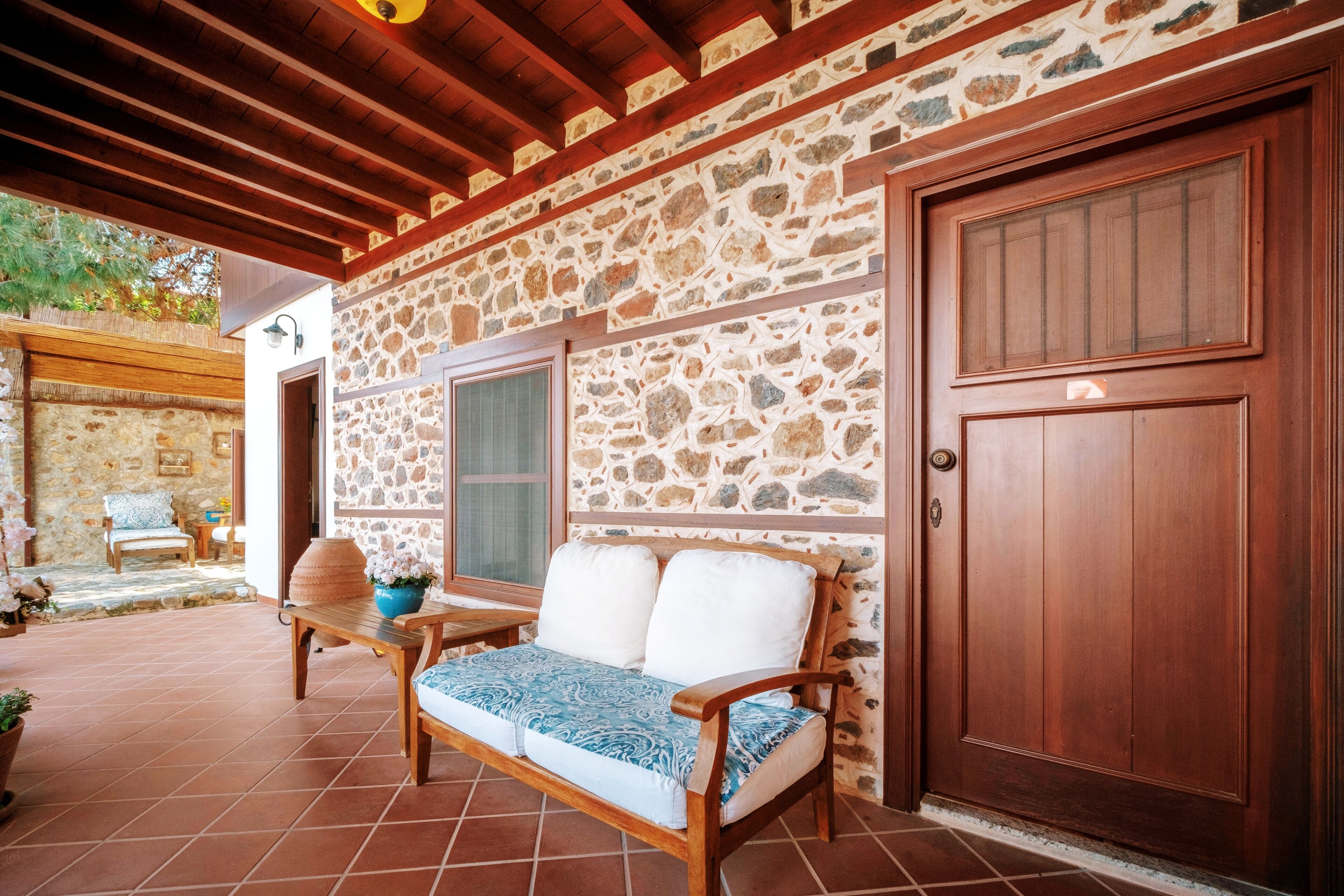 A covered patio with a stone wall, wooden bench, and a door.