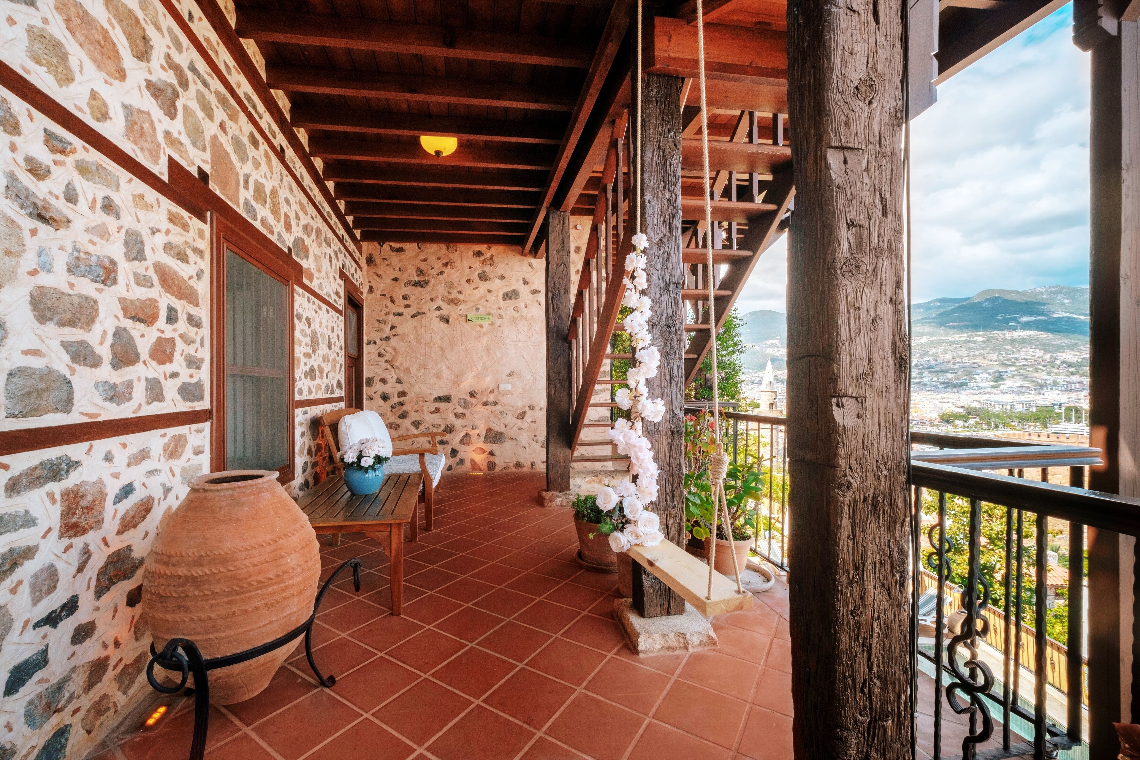 A stone-walled balcony with a rustic wooden ceiling, a large terracotta pot, and a wooden bench.