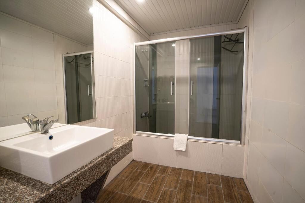 Un baño con un lavamanos grande de color blanco, cabina de ducha de vidrio y suelo con baldosas.