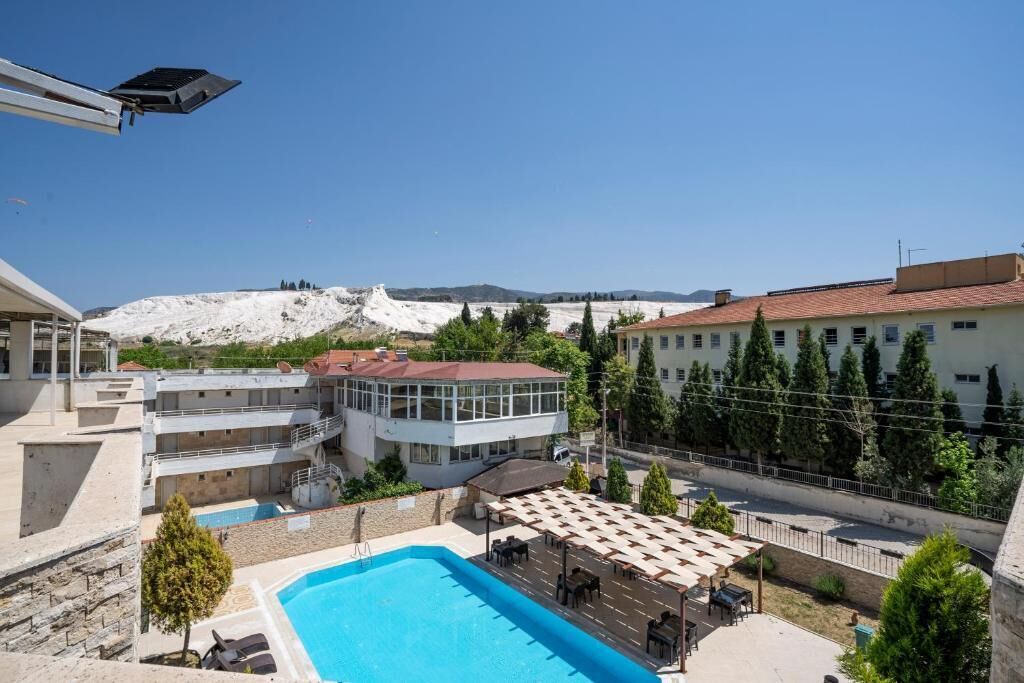 A hotel with a swimming pool, outdoor seating, and a view of a mountainous landscape.