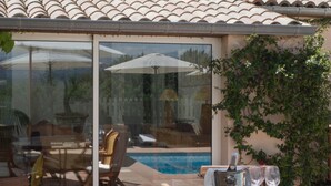 Un área junto a la piscina con puerta de vidrio, mobiliario exterior y una mesa con un balde y vasos de metal.