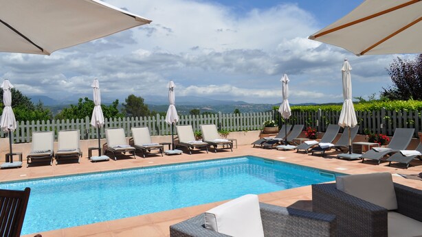 Zona de piscina con sillones y sombrillas, una valla de madera y vistas a montañas distantes.
