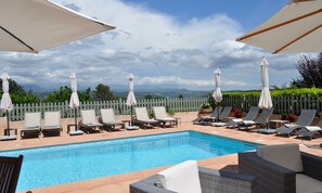 A poolside area with lounge chairs and umbrellas, a wooden fence, and a view of distant mountains. - La Bégude du Pascouren (Fayence)