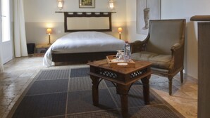Una habitación de hotel con una cama, una mesita de noche de madera, una silla, dos lámparas de noche y un cuadro colgado en la pared.