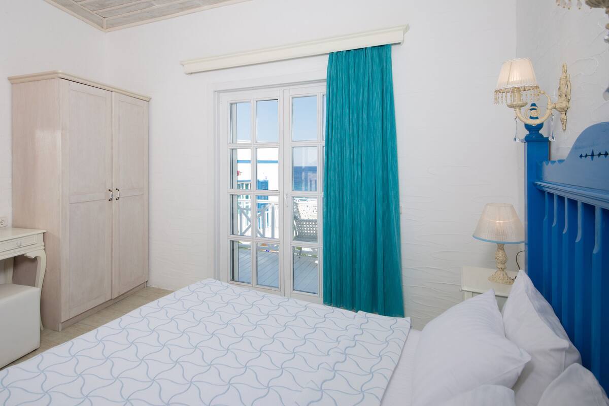 A bedroom with a bed, a dresser, a mirror, a window with curtains, and a balcony view.