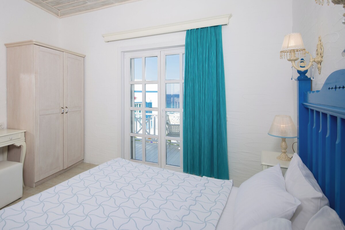 A bedroom with a bed, a dresser, a mirror, a window with curtains, and a balcony view.