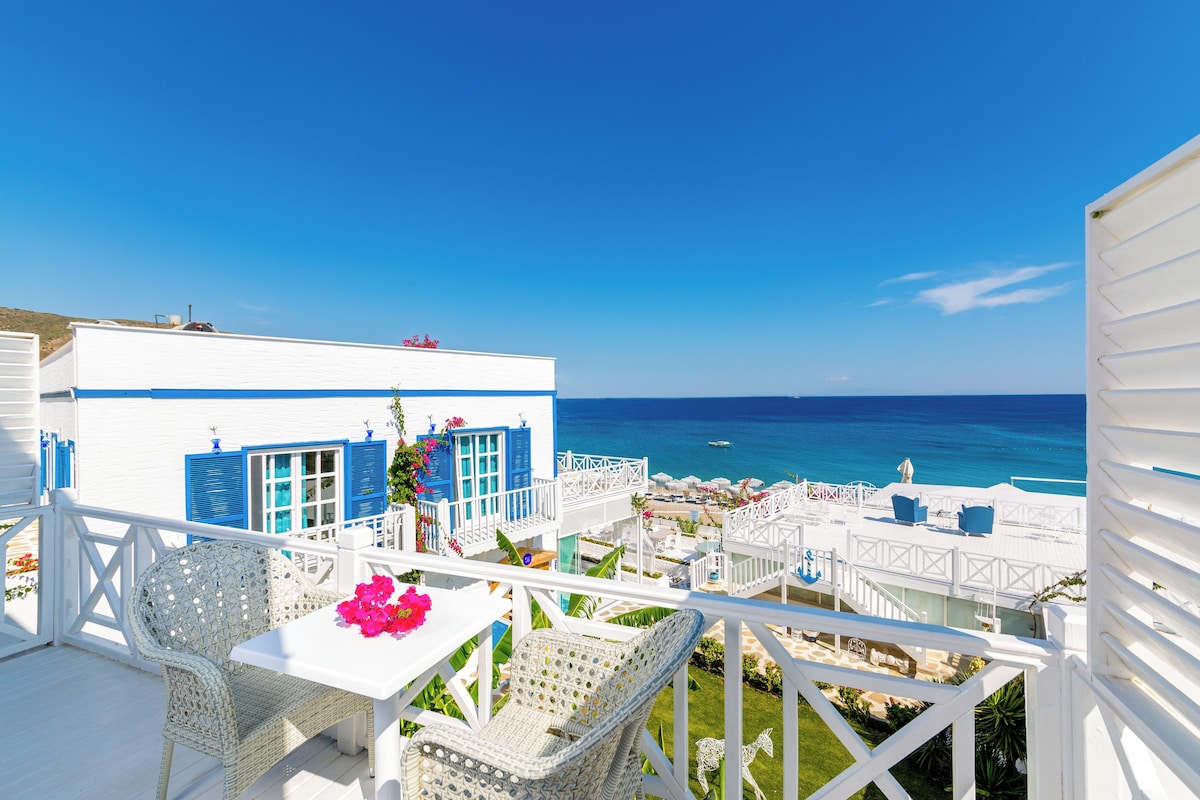 A white building with blue shutters, wicker furniture, and a view of the sea.