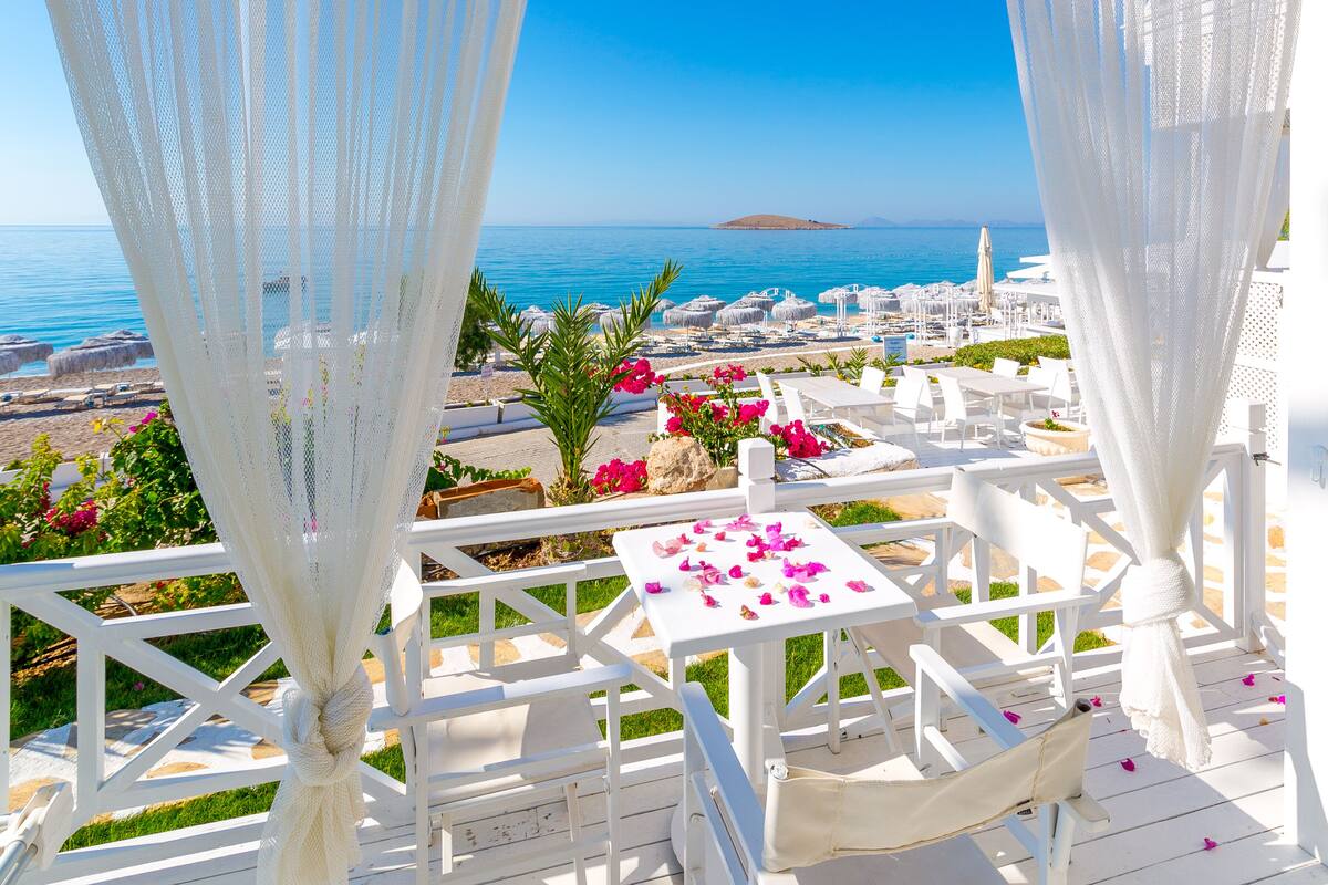 A terrace with white furniture, a view of the sea, and a white pergola.