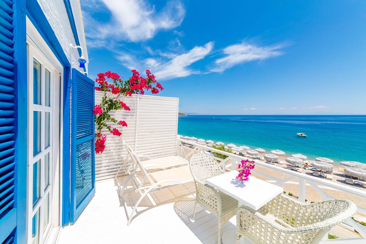 A balcony with white wicker furniture, a table with a vase of flowers, and a view of the sea.