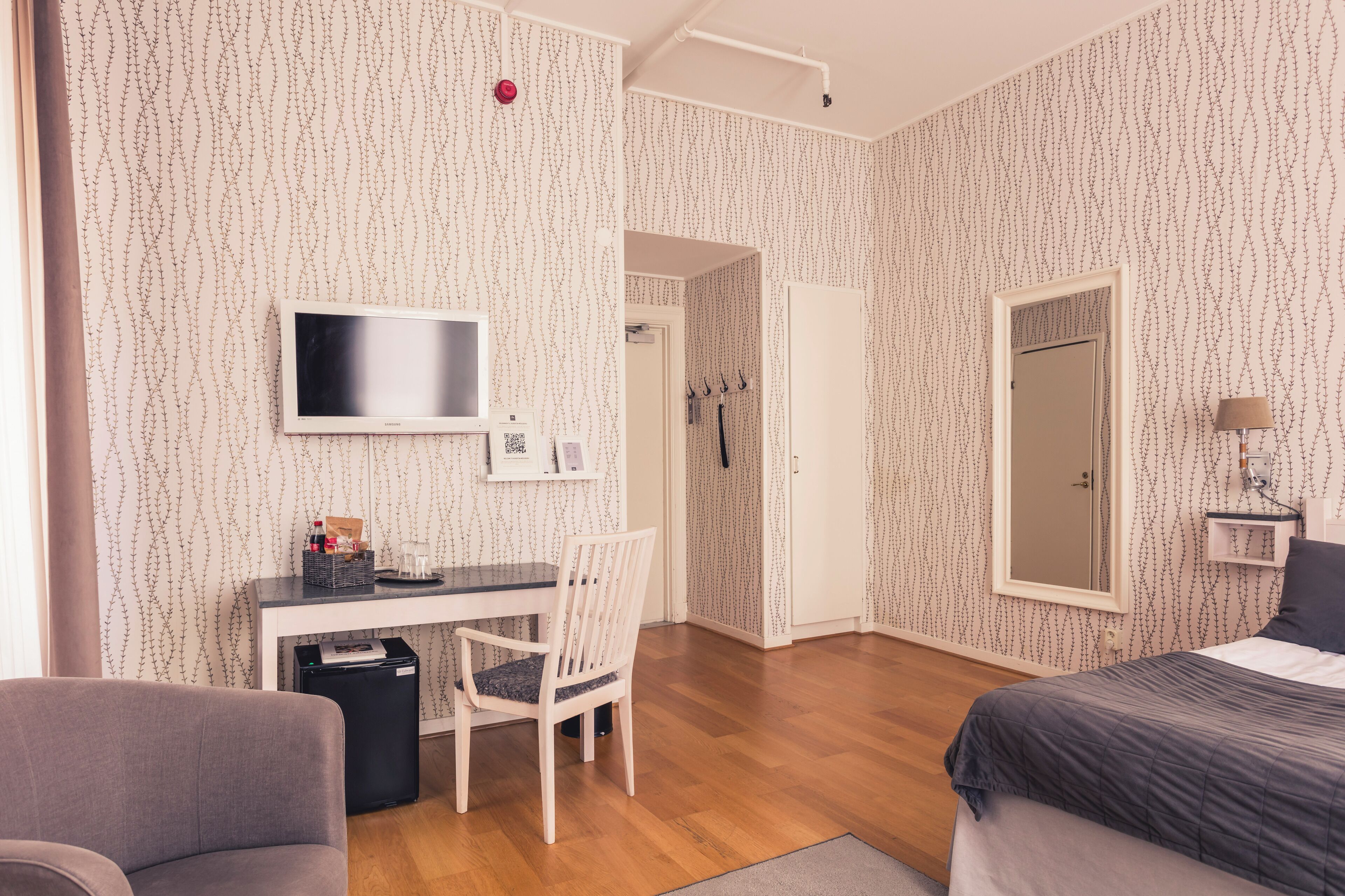 Ett hotellrum med ett skrivbord, en stol, en säng och en tv som är monterad på väggen.