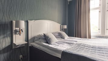 A neatly made bed with white linens and pillows, a white headboard, and a bedside table with a lamp.