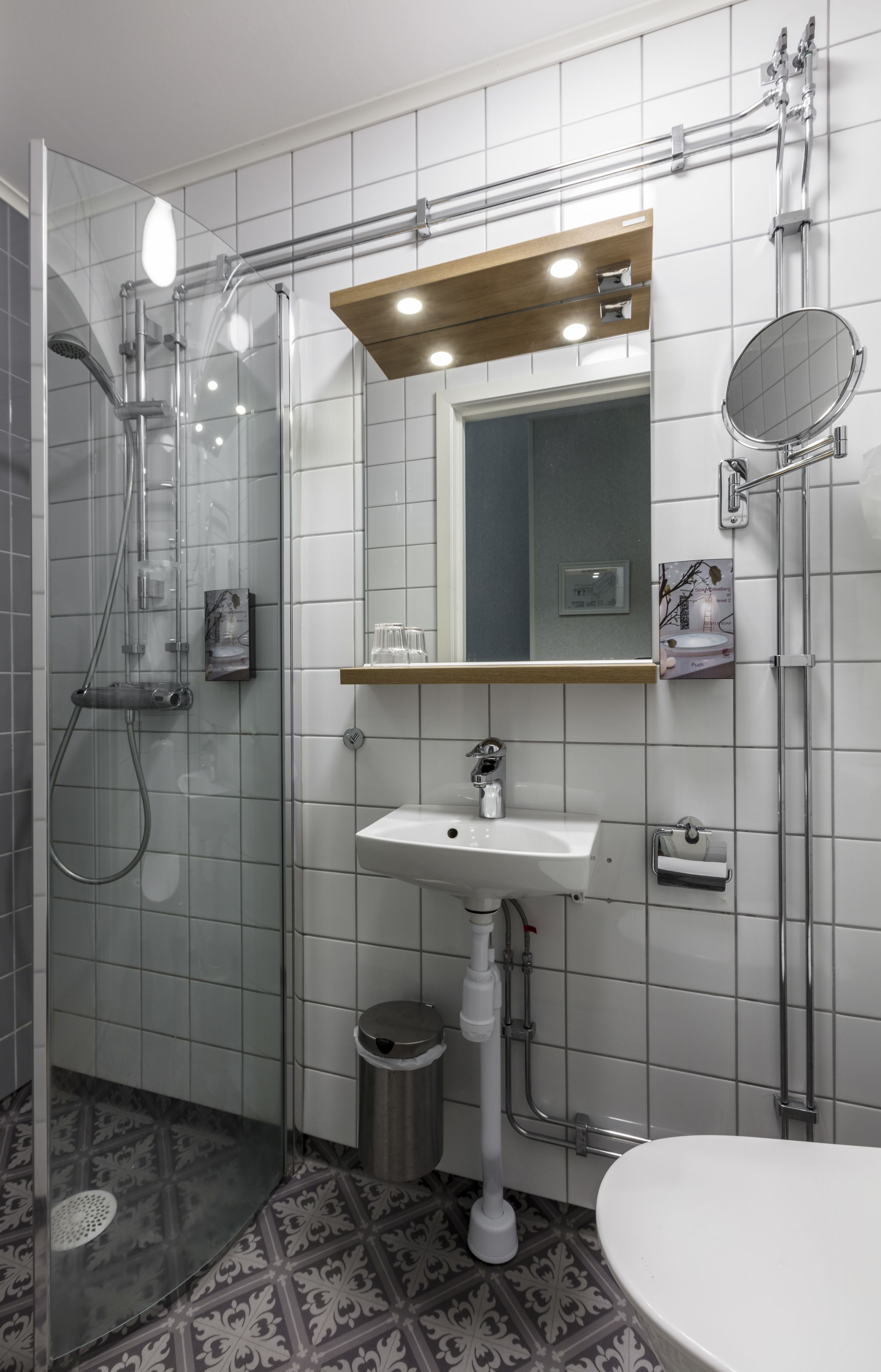 Un baño moderno con ducha de vidrio, lavamanos pedestal, espejo y retrete.