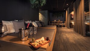 Una habitación de hotel moderna con un banco de madera, un minibar y una zona de estar con sofá y sillones.